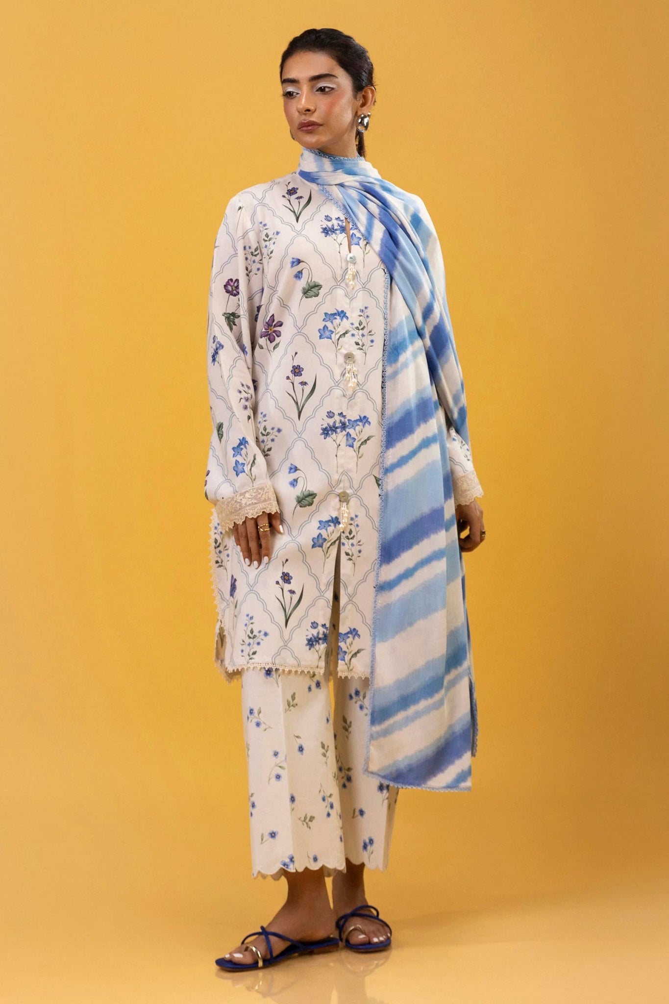 Model wearing a three - piece outfit from the Mahay Winter '24 collection by Sana Safinaz. The digitally printed linen shirt features a coordinated front, back, and sleeves with delicate embroidered patti on organza. Paired with rotary - printed cambric pants and a matching printed linen dupatta. Available online in the UK.