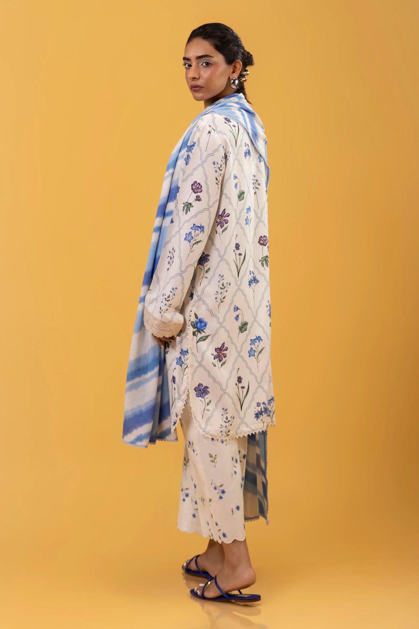 Model wearing a three - piece outfit from the Mahay Winter '24 collection by Sana Safinaz. The digitally printed linen shirt features a coordinated front, back, and sleeves with delicate embroidered patti on organza. Paired with rotary - printed cambric pants and a matching printed linen dupatta. Available online in the UK.