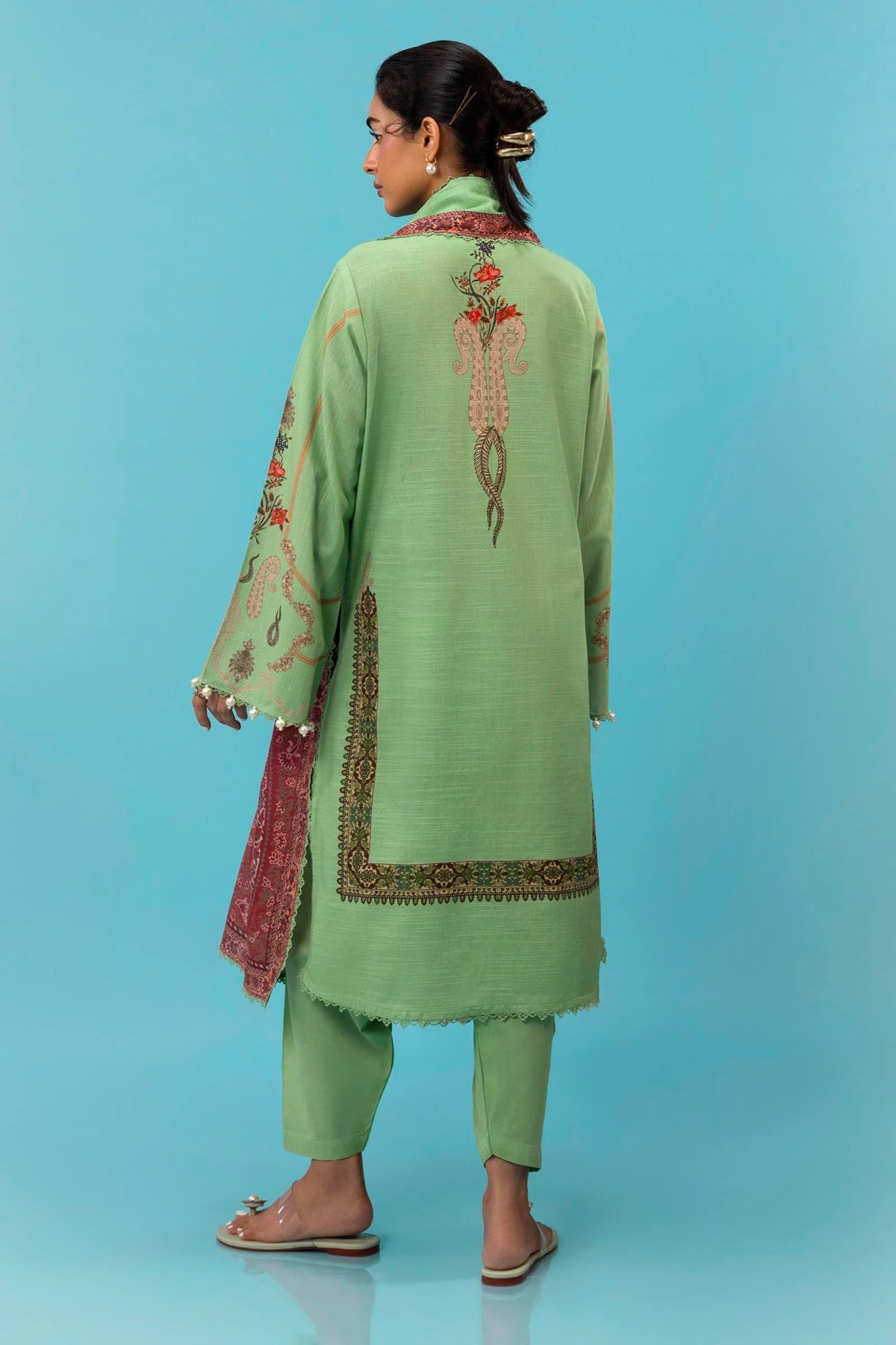 A model is wearing a three - piece outfit from the Mahay Winter '24 collection by Sana Safinaz. This ensemble includes a digitally printed slub shirt with coordinated front, back, and sleeves, and an embroidered organza neckline for added elegance. It is paired with dyed cambric pants and a digitally printed khaddar dupatta, completing the look with rich patterns. Ideal for women seeking premium Pakistani fashion, this outfit is available online in the UK for £64.00.