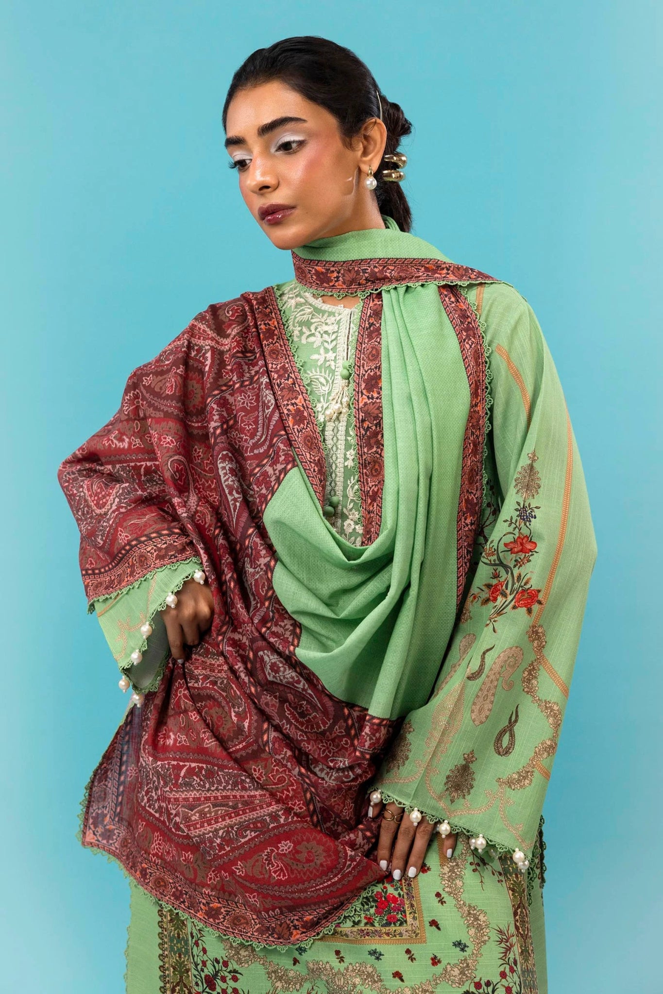 A model is wearing a three - piece outfit from the Mahay Winter '24 collection by Sana Safinaz. This ensemble includes a digitally printed slub shirt with coordinated front, back, and sleeves, and an embroidered organza neckline for added elegance. It is paired with dyed cambric pants and a digitally printed khaddar dupatta, completing the look with rich patterns. Ideal for women seeking premium Pakistani fashion, this outfit is available online in the UK for £64.00.