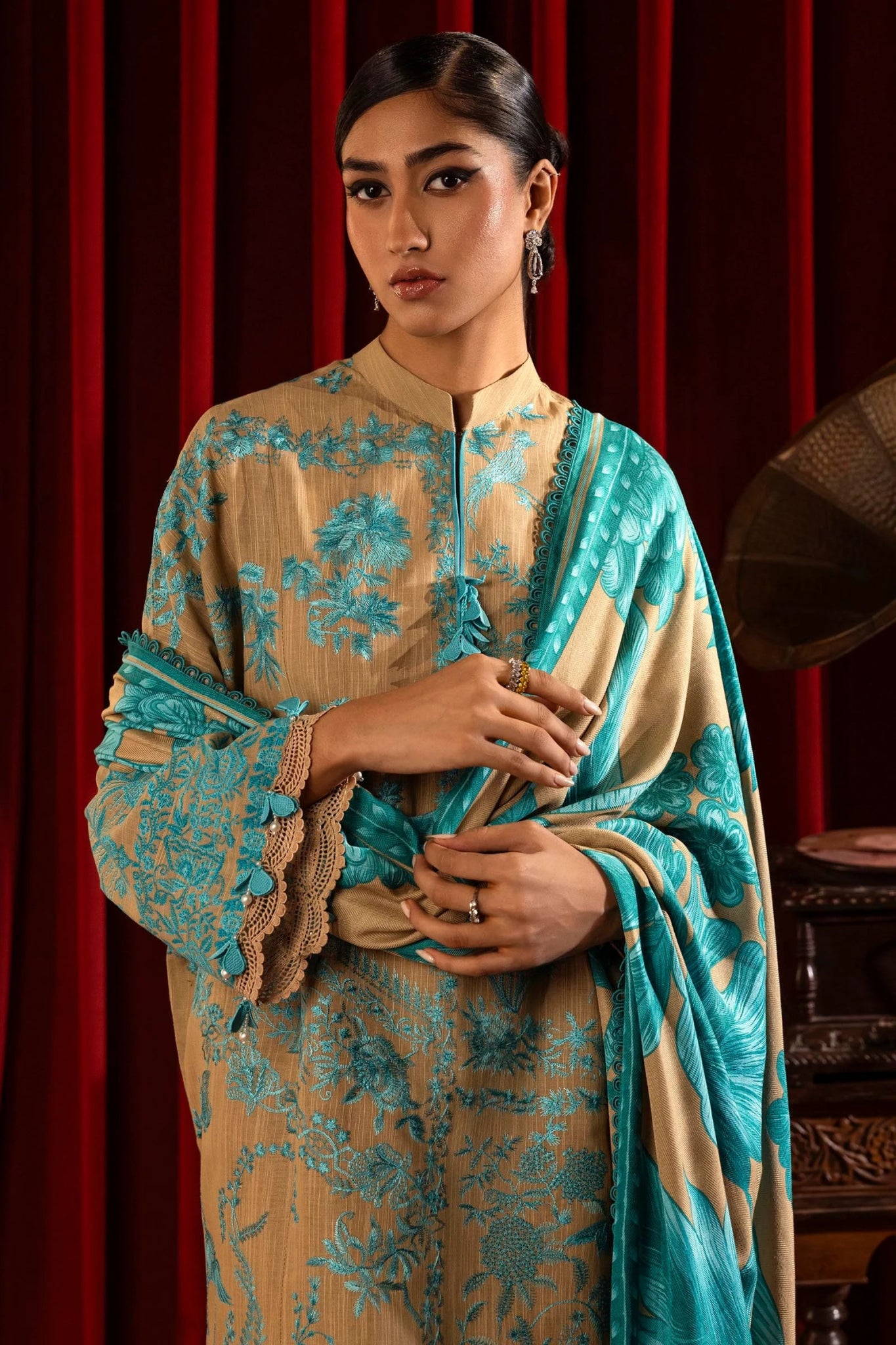 A model wears a three - piece outfit from the Sana Safinaz Muzlin Winter '24 Collection. The ensemble features intricately embroidered front panels on slub fabric, complemented by a printed back and sleeves. It is paired with a matching 2.5 - meter printed shawl and dyed cotton pants, creating a sophisticated winter look. Available online in the UK.