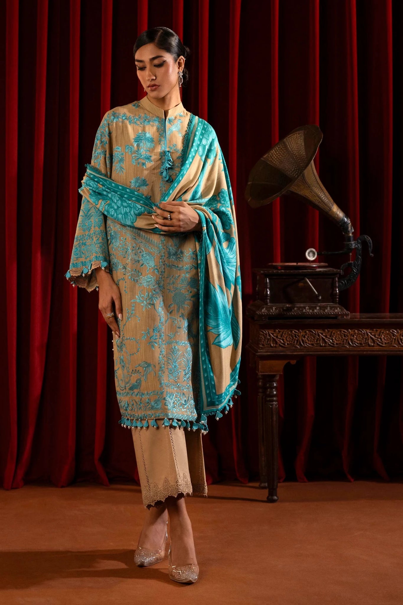 A model wears a three - piece outfit from the Sana Safinaz Muzlin Winter '24 Collection. The ensemble features intricately embroidered front panels on slub fabric, complemented by a printed back and sleeves. It is paired with a matching 2.5 - meter printed shawl and dyed cotton pants, creating a sophisticated winter look. Available online in the UK.