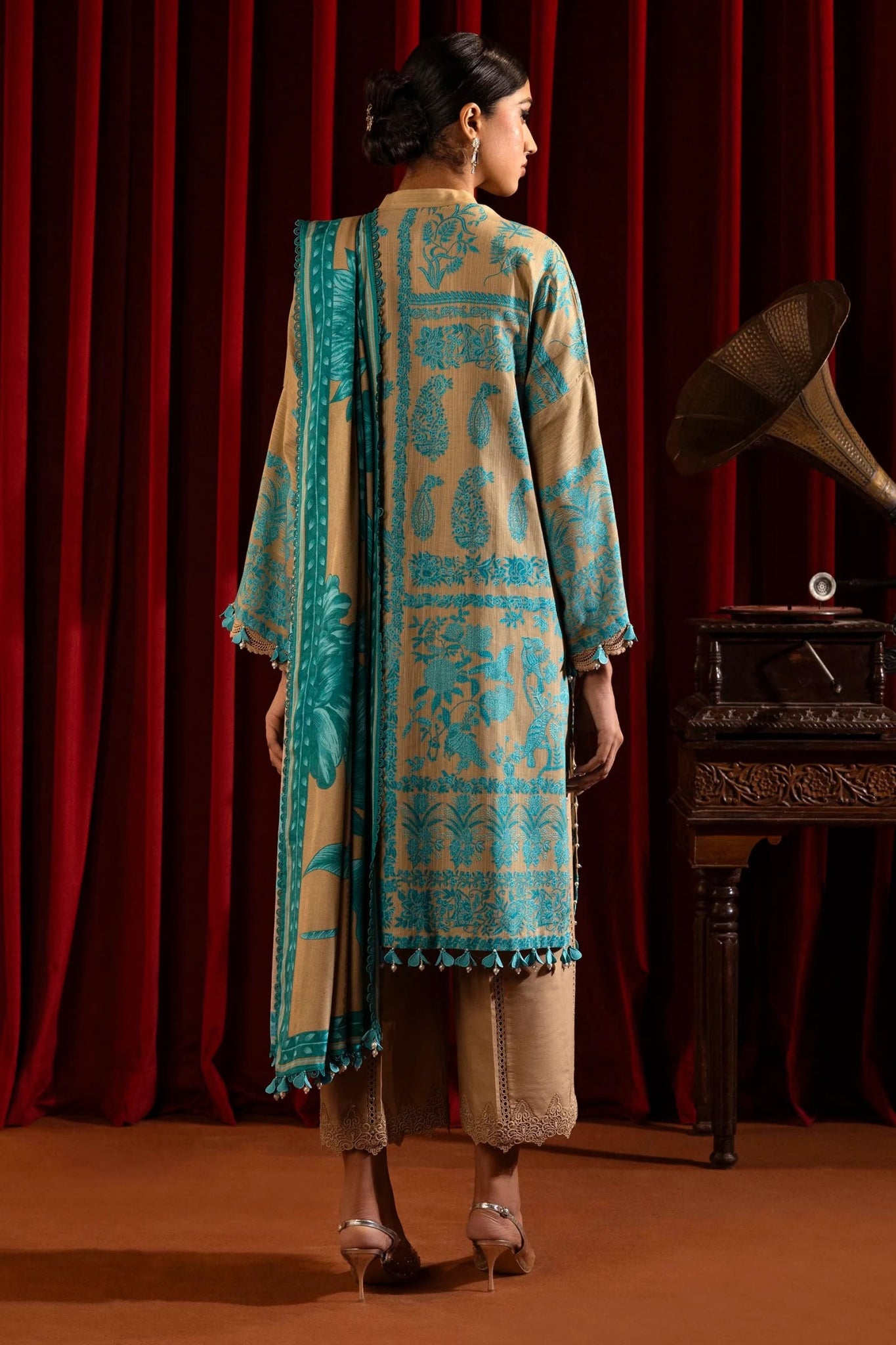 A model wears a three - piece outfit from the Sana Safinaz Muzlin Winter '24 Collection. The ensemble features intricately embroidered front panels on slub fabric, complemented by a printed back and sleeves. It is paired with a matching 2.5 - meter printed shawl and dyed cotton pants, creating a sophisticated winter look. Available online in the UK.