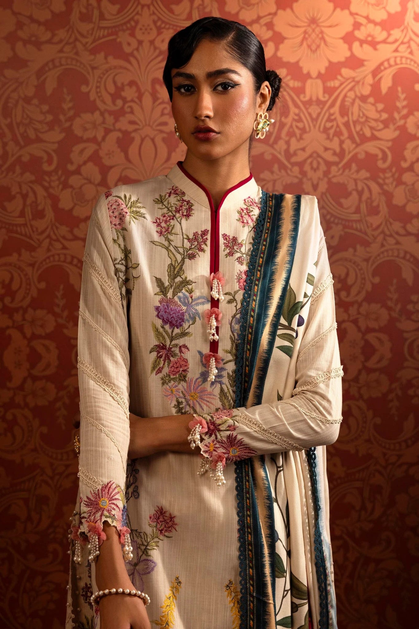 A model wears a luxurious three - piece outfit from the Sana Safinaz Muzlin Winter '24 Collection. The ensemble features intricately embroidered front kalis on slub fabric, complemented by dyed slub sleeves and back. It includes a vibrant digital printed shawl and matching dyed cotton pants, creating an elegant look perfect for women seeking stylish Pakistani designer clothing. Available online in the UK.