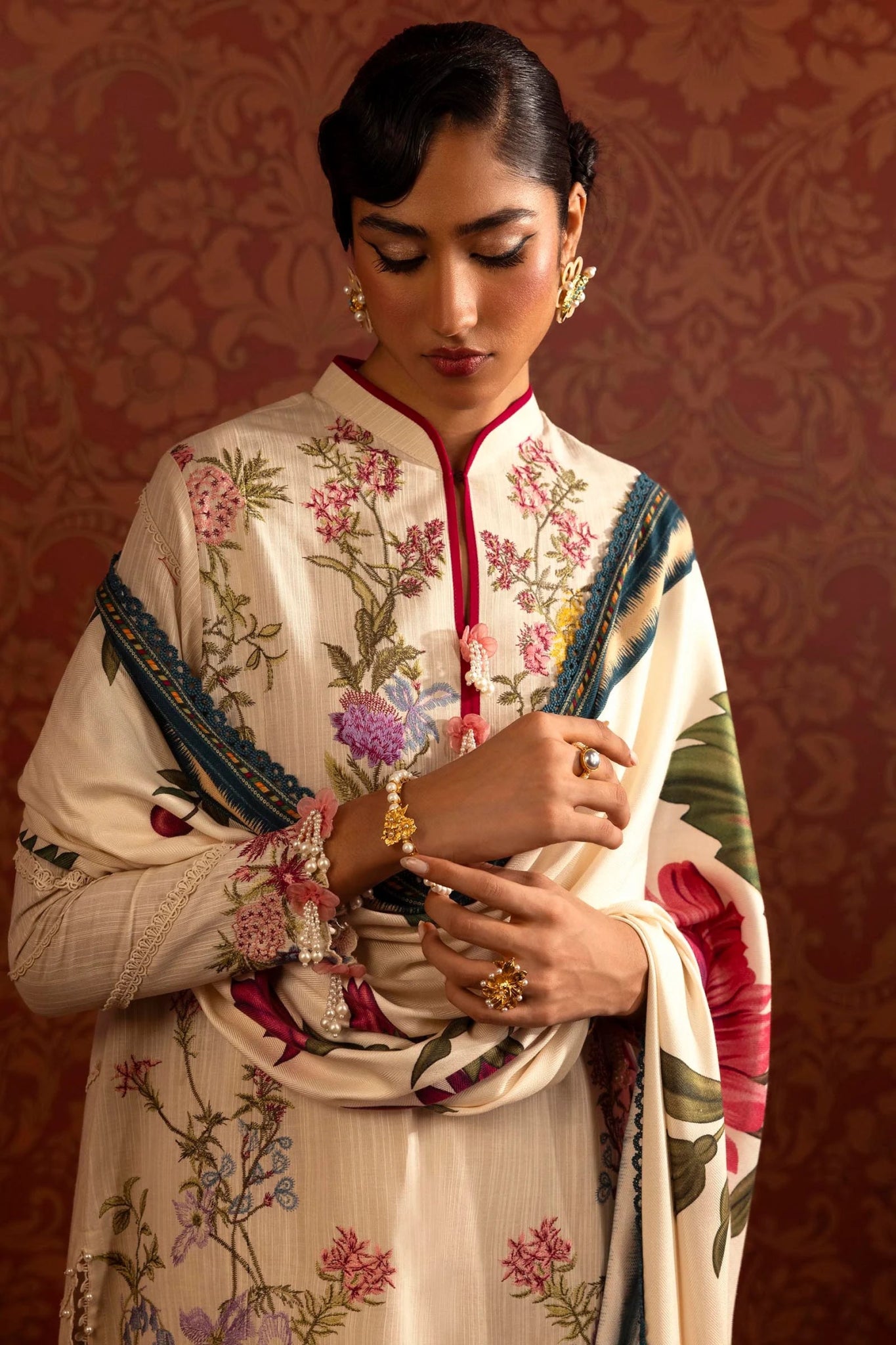 A model wears a luxurious three - piece outfit from the Sana Safinaz Muzlin Winter '24 Collection. The ensemble features intricately embroidered front kalis on slub fabric, complemented by dyed slub sleeves and back. It includes a vibrant digital printed shawl and matching dyed cotton pants, creating an elegant look perfect for women seeking stylish Pakistani designer clothing. Available online in the UK.