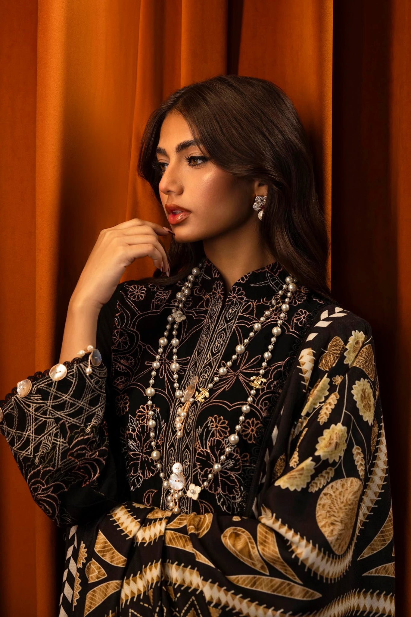 A model wears a three - piece outfit from the Sana Safinaz Muzlin Winter '24 Collection. The ensemble features an embroidered slub shirt with front kali panels, dyed slub back, and embroidered sleeves. Paired with a digitally printed shawl showcasing intricate patterns and dyed cotton pants, this luxurious Pakistani outfit blends traditional embroidery with contemporary design.