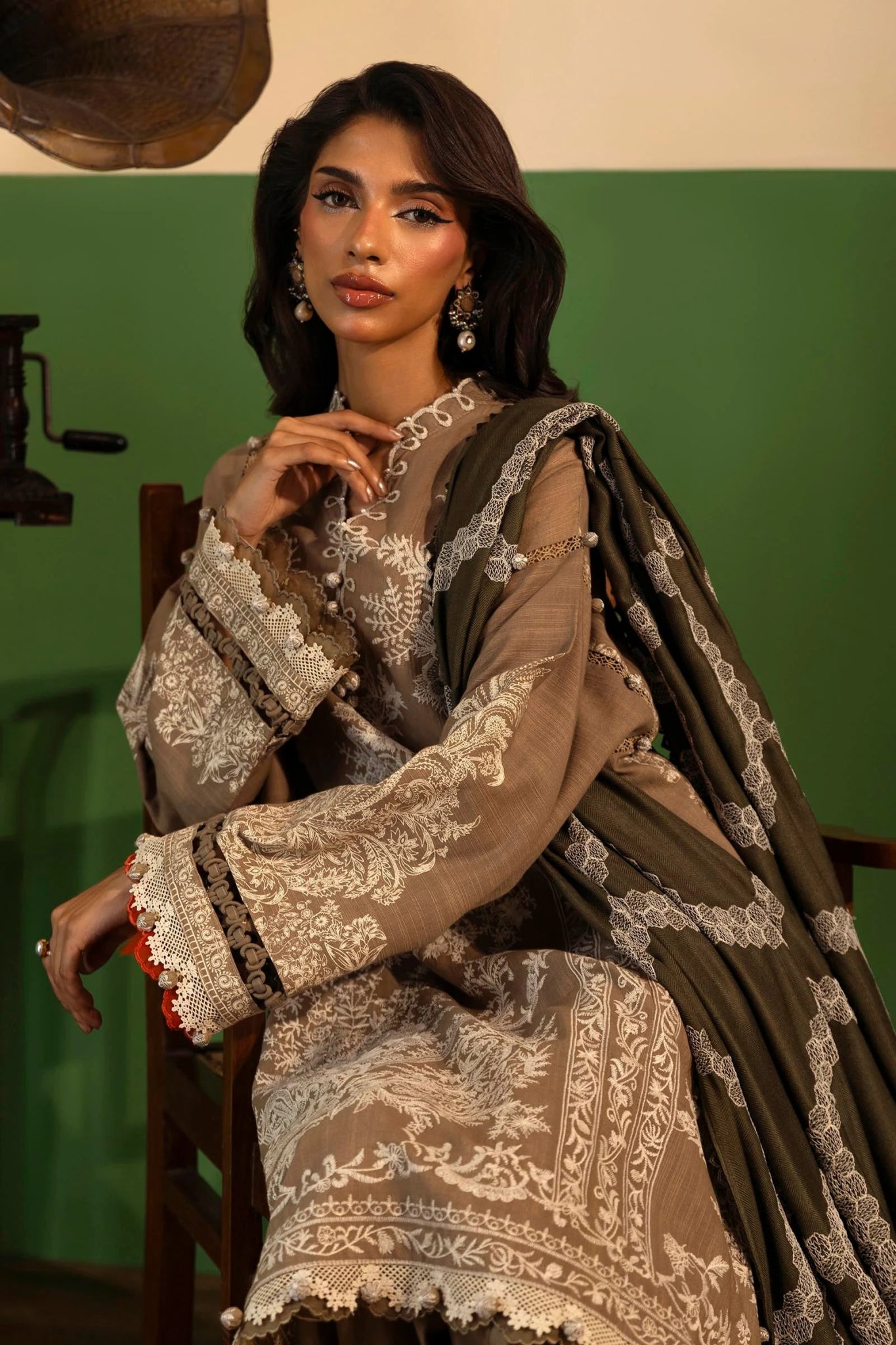 A model showcases a three - piece outfit from the Sana Safinaz Muzlin Winter '24 Collection. The ensemble features an embroidered front kali on slub, paired with a printed slub back and sleeves. Embroidered organza patti adorns the neckline and sleeves, while an intricately embroidered shawl complements the look. Dyed cotton pants complete the outfit for an elegant winter style. Perfect for women seeking premium Pakistani designer wear.