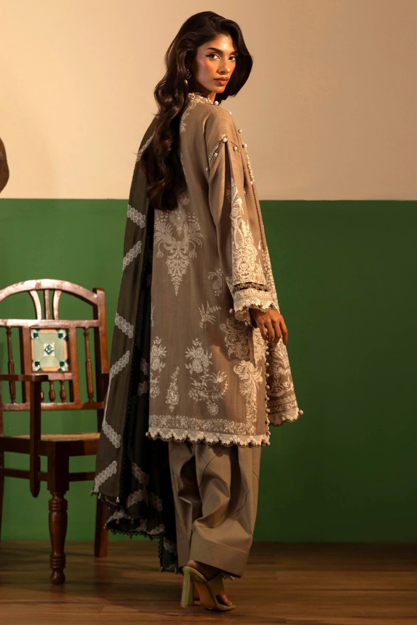 A model showcases a three - piece outfit from the Sana Safinaz Muzlin Winter '24 Collection. The ensemble features an embroidered front kali on slub, paired with a printed slub back and sleeves. Embroidered organza patti adorns the neckline and sleeves, while an intricately embroidered shawl complements the look. Dyed cotton pants complete the outfit for an elegant winter style. Perfect for women seeking premium Pakistani designer wear.