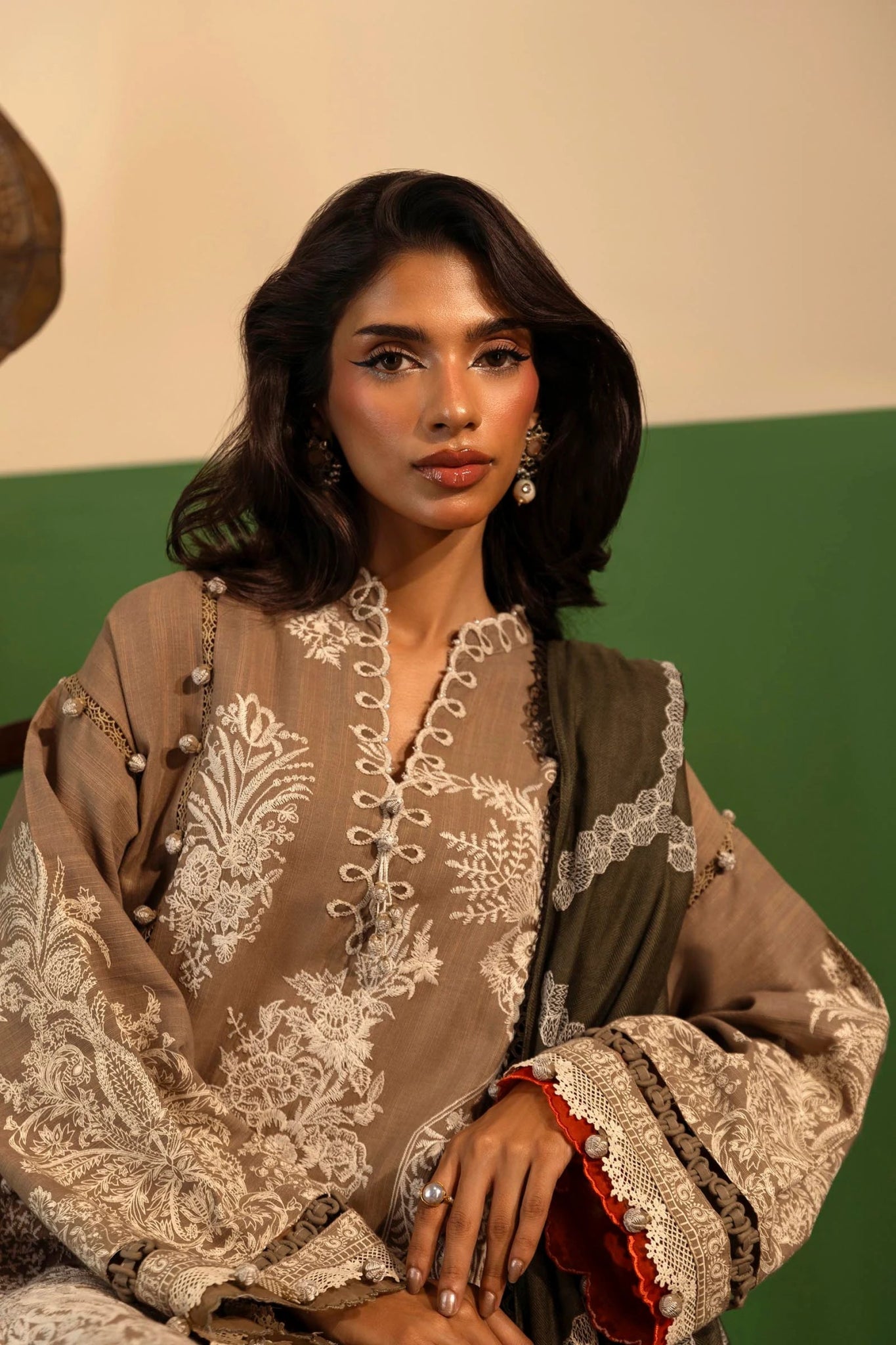 A model showcases a three - piece outfit from the Sana Safinaz Muzlin Winter '24 Collection. The ensemble features an embroidered front kali on slub, paired with a printed slub back and sleeves. Embroidered organza patti adorns the neckline and sleeves, while an intricately embroidered shawl complements the look. Dyed cotton pants complete the outfit for an elegant winter style. Perfect for women seeking premium Pakistani designer wear.