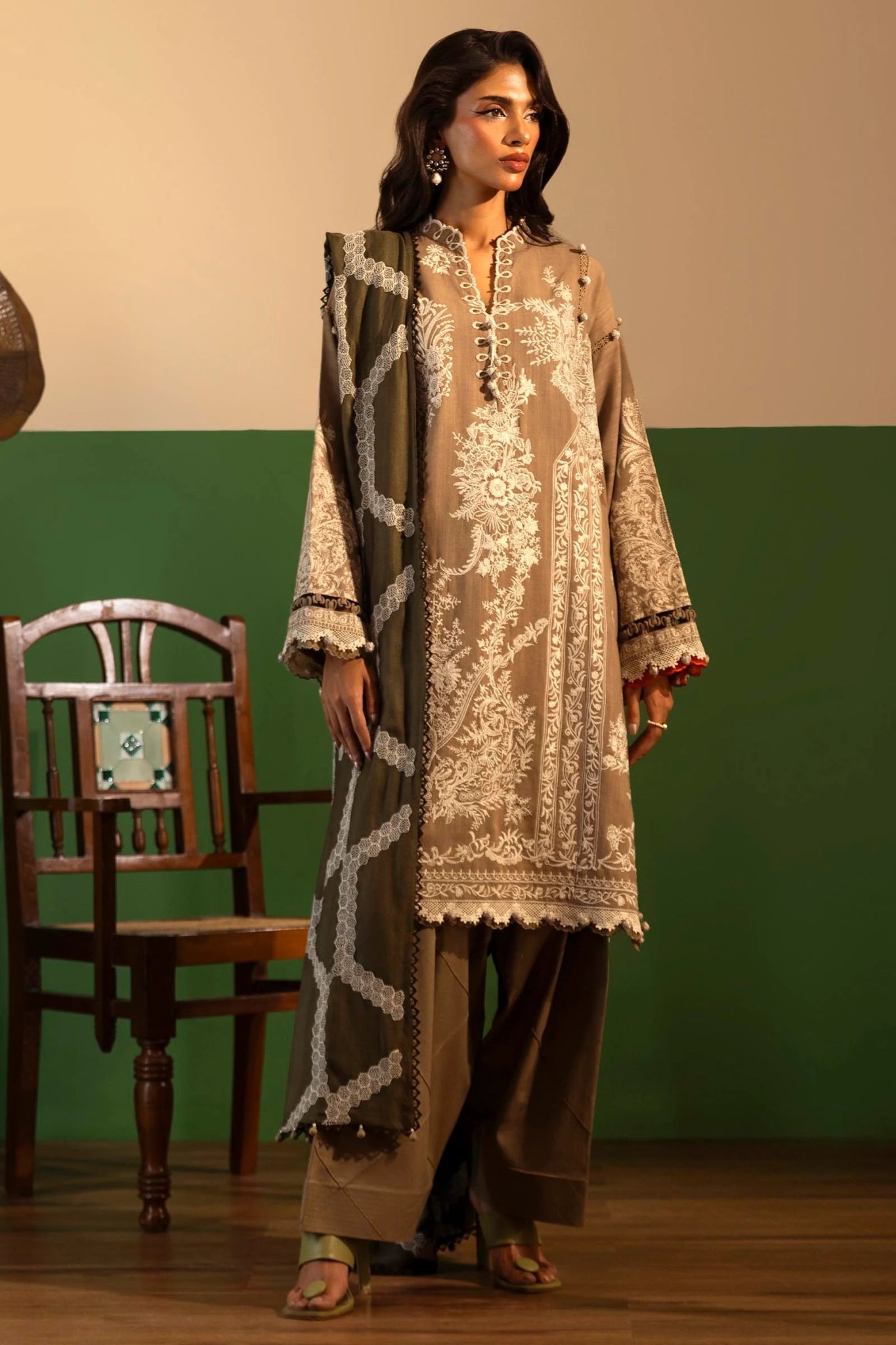 A model showcases a three - piece outfit from the Sana Safinaz Muzlin Winter '24 Collection. The ensemble features an embroidered front kali on slub, paired with a printed slub back and sleeves. Embroidered organza patti adorns the neckline and sleeves, while an intricately embroidered shawl complements the look. Dyed cotton pants complete the outfit for an elegant winter style. Perfect for women seeking premium Pakistani designer wear.