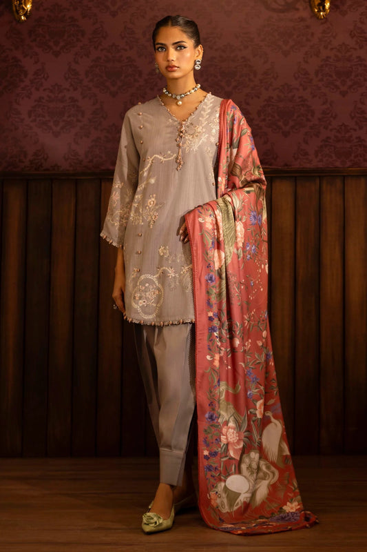 A model wears a three - piece outfit from the Sana Safinaz Muzlin Winter '24 Collection. It features an embroidered front kali on slub, printed back, and embroidered sleeves, paired with a vibrant, digitally printed shawl and matching dyed cotton pants. This elegant look blends traditional embroidery with a modern flair, ideal for women seeking premium Pakistani fashion online in the UK.