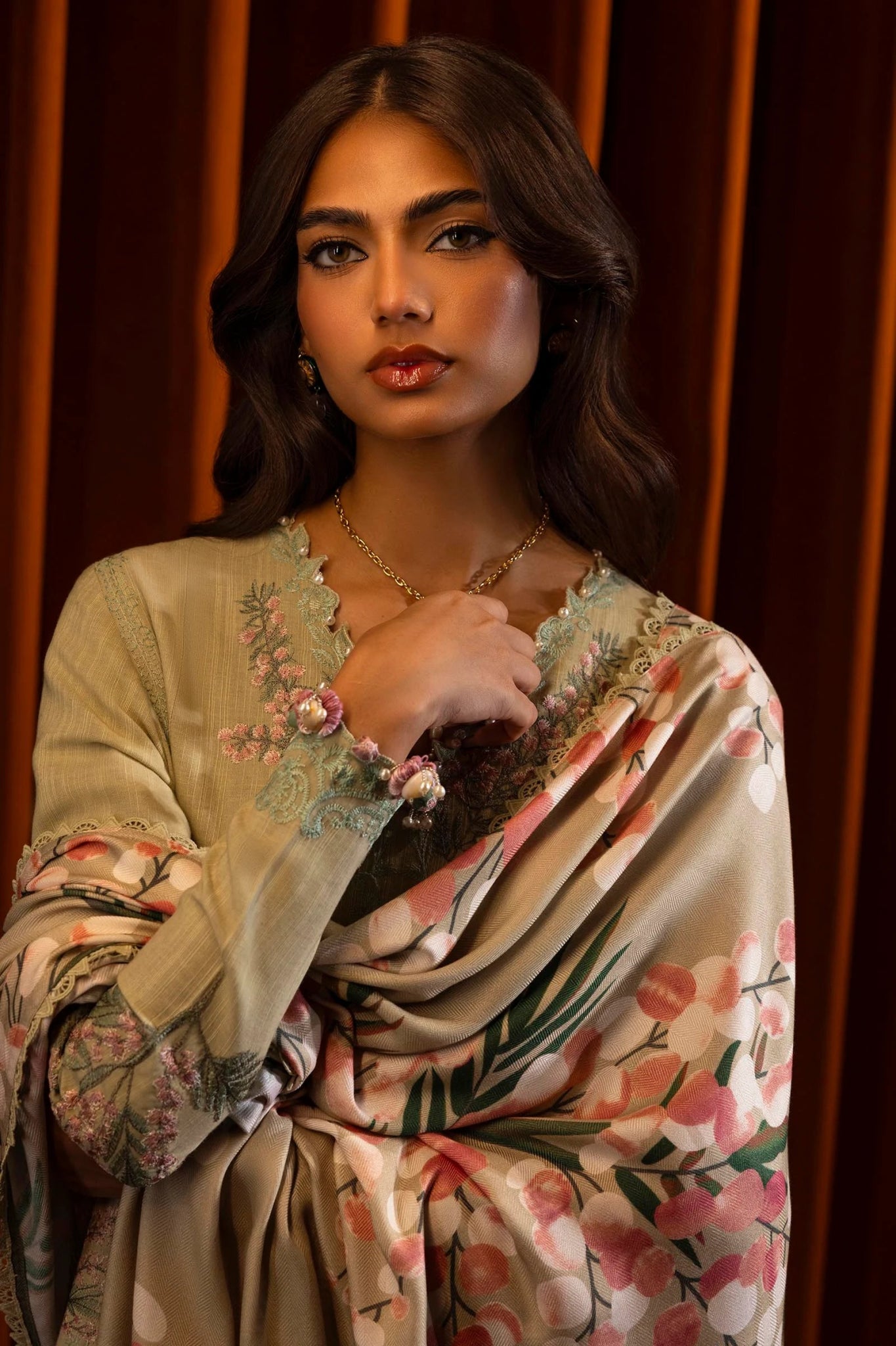 A model wears a three - piece outfit from the Sana Safinaz Muzlin Winter '24 Collection. This ensemble includes an embroidered front kali on slub fabric, a dyed back, and embroidered sleeves with organza kuful details. The look is complemented by a digital printed shawl and dyed cotton pants, offering an elegant and cohesive style. Perfect for women seeking luxurious Pakistani designer clothing in the UK.