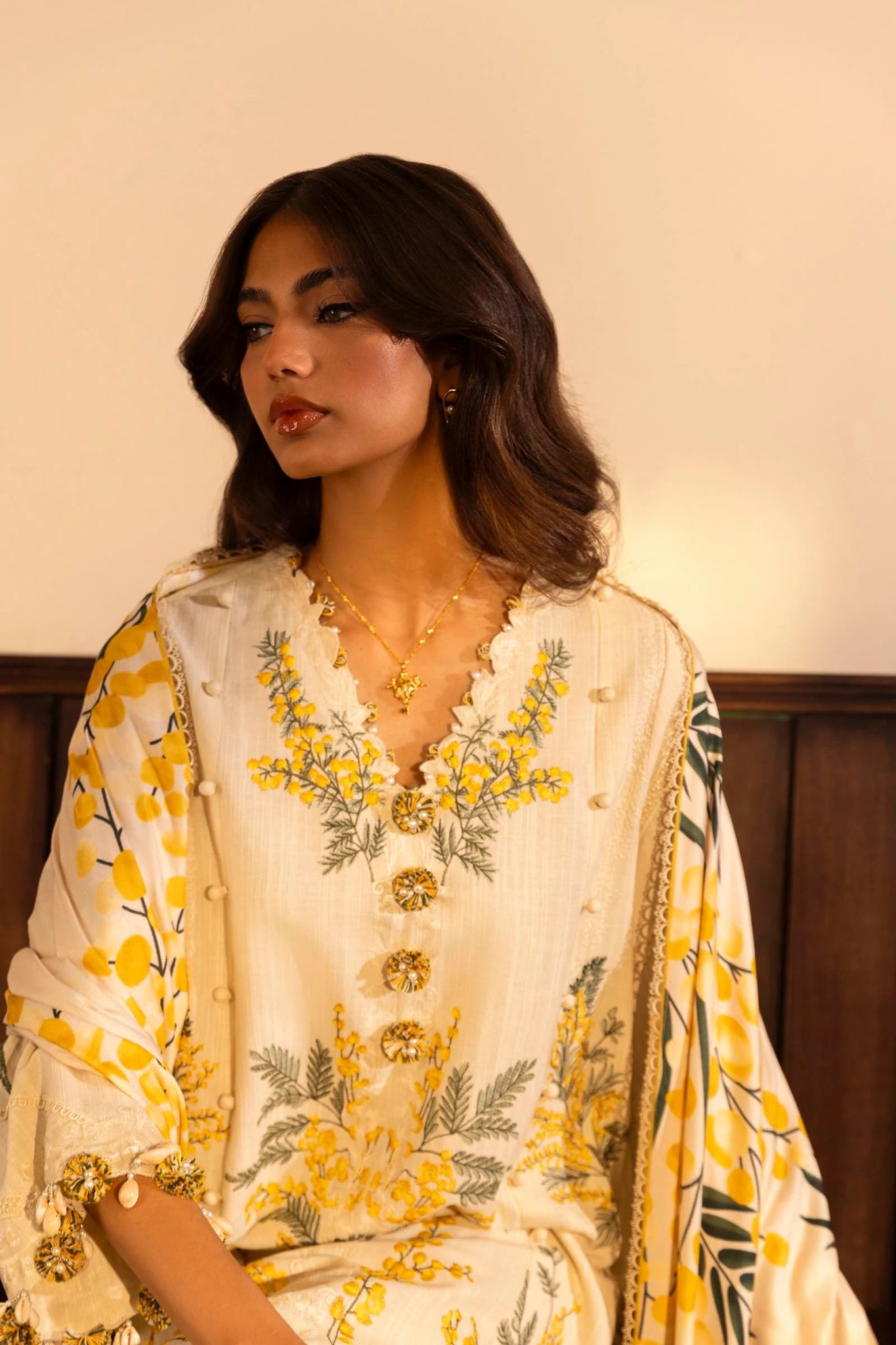 A model is wearing a three - piece outfit from the Sana Safinaz Muzlin Winter '24 Collection. The ensemble features an embroidered front kali on slub fabric, paired with a dyed slub back and sleeves, accentuated by organza embroidered kuful. The look is completed with a vibrant, digitally printed shawl and dyed cotton pants, combining traditional elegance with a modern aesthetic. Perfect for women seeking luxurious Pakistani designer clothing in the UK.