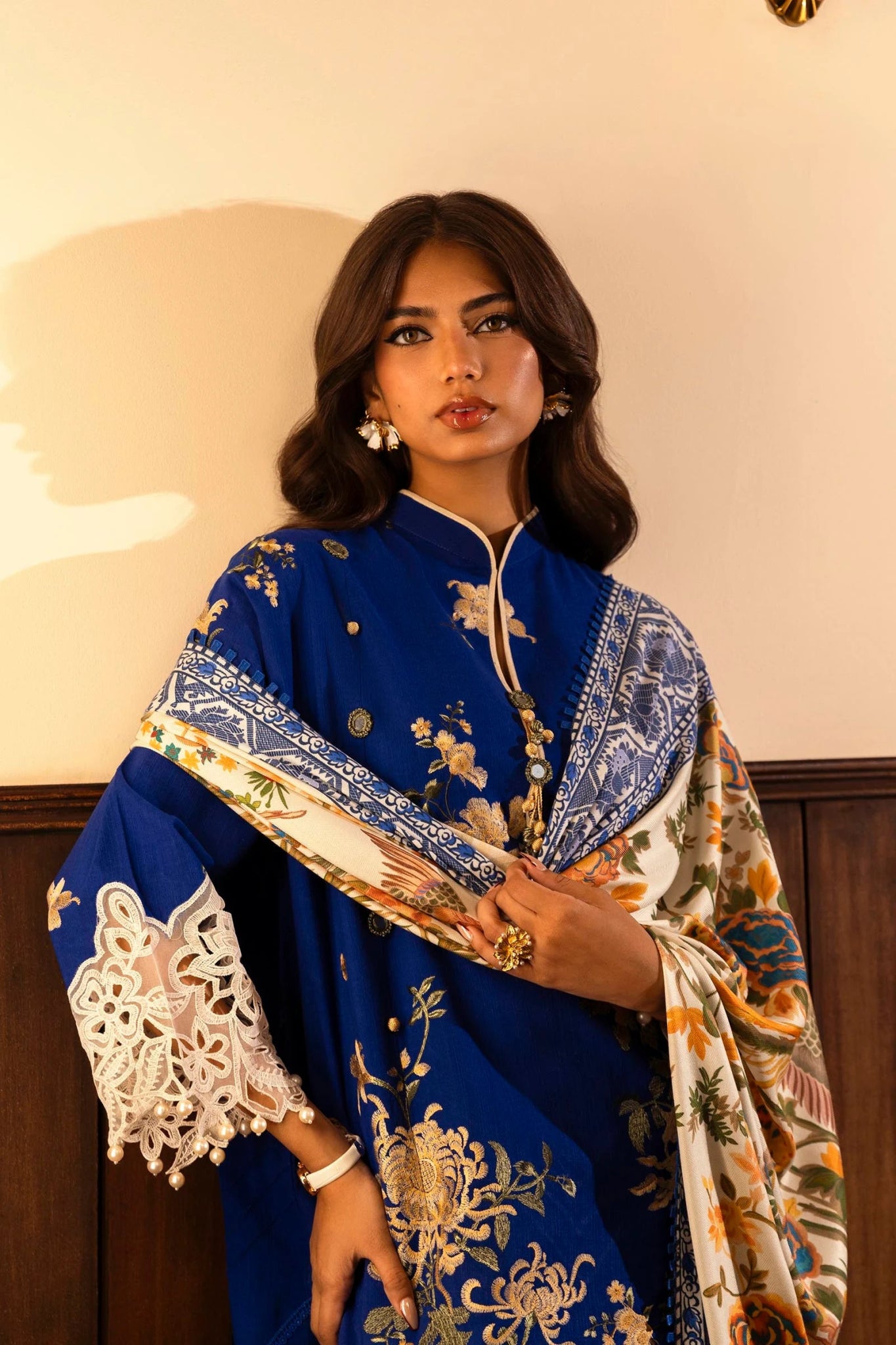 A model wears a three - piece outfit from the Sana Safinaz Muzlin Winter '24 Collection. The ensemble features an embroidered slub front kali with intricate detailing on the sleeves and borders. It includes a vibrant digital - printed shawl and dyed cotton pants for a complete look. Ideal for women seeking luxurious and elegant Pakistani fashion.