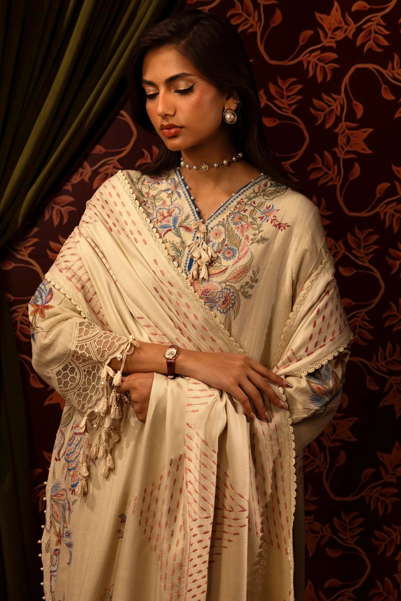 A model showcases a three - piece outfit from the Sana Safinaz Muzlin Winter '24 Collection. The design includes an embroidered front kali on slub in three pieces, paired with a dyed slub back and matching embroidered sleeves. The ensemble is completed with a delicate embroidered organza kuful, a detailed embroidered shawl, and coordinating dyed cotton pants. Ideal for a luxurious and sophisticated look.