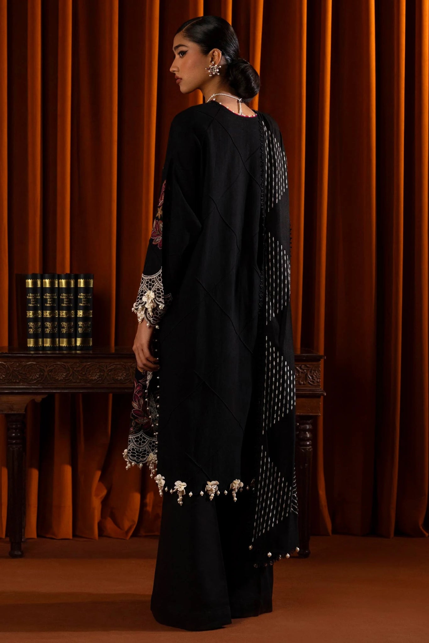 Model wearing a 3 - piece black embroidered suit by a Pakistani designer, featuring a slub front kali, organza kuful details, intricate embroidered shawl, and dyed cotton pants, styled elegantly. Available online in the UK.