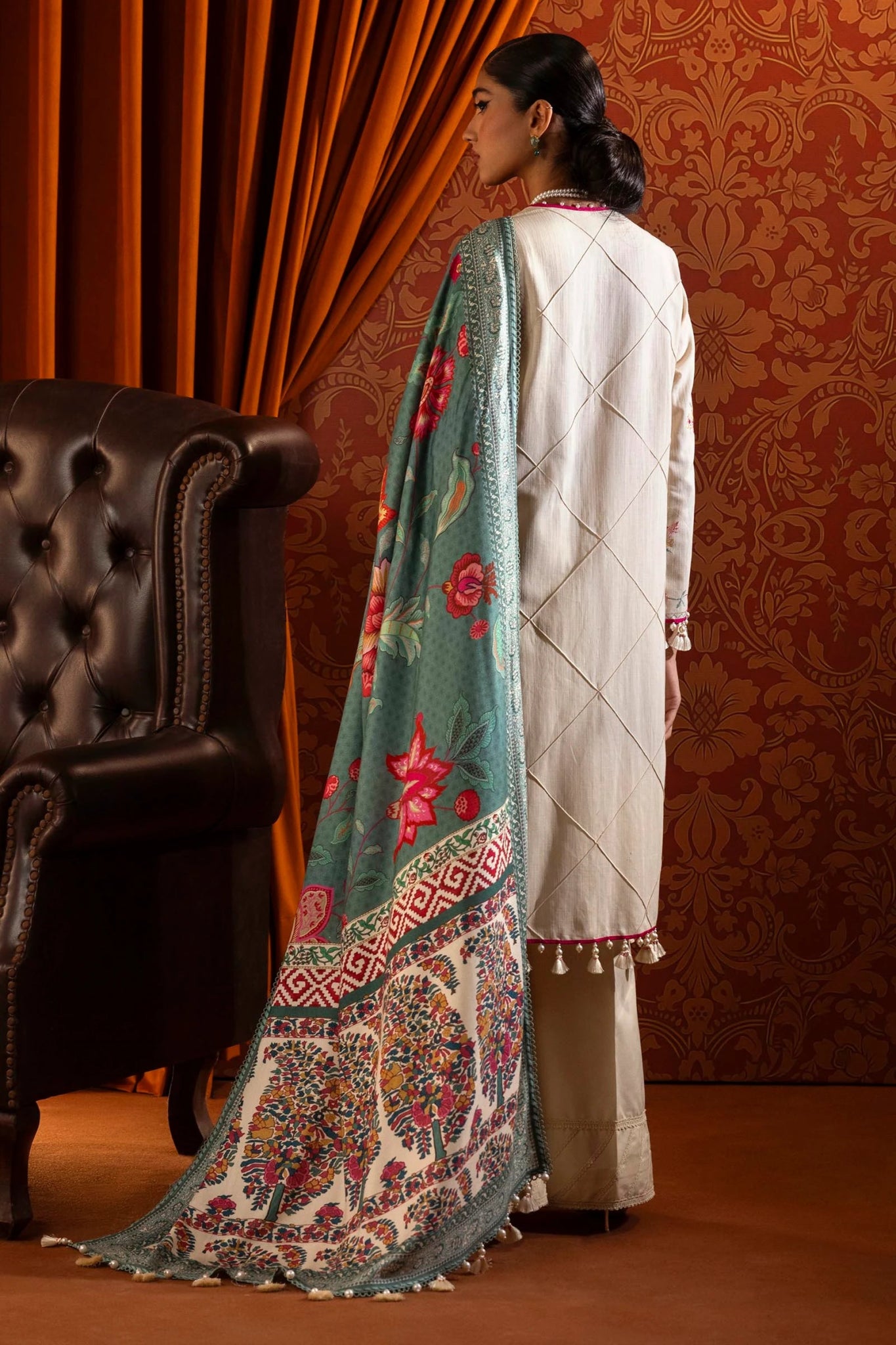 Model wearing a 3 - piece off - white embroidered suit featuring a slub front kali, embroidered sleeves, and a digitally printed shawl with vibrant patterns. Paired with dyed cotton pants, styled gracefully. Part of the Sana Safinaz Muzlin Winter 2024 collection, available online in the UK."