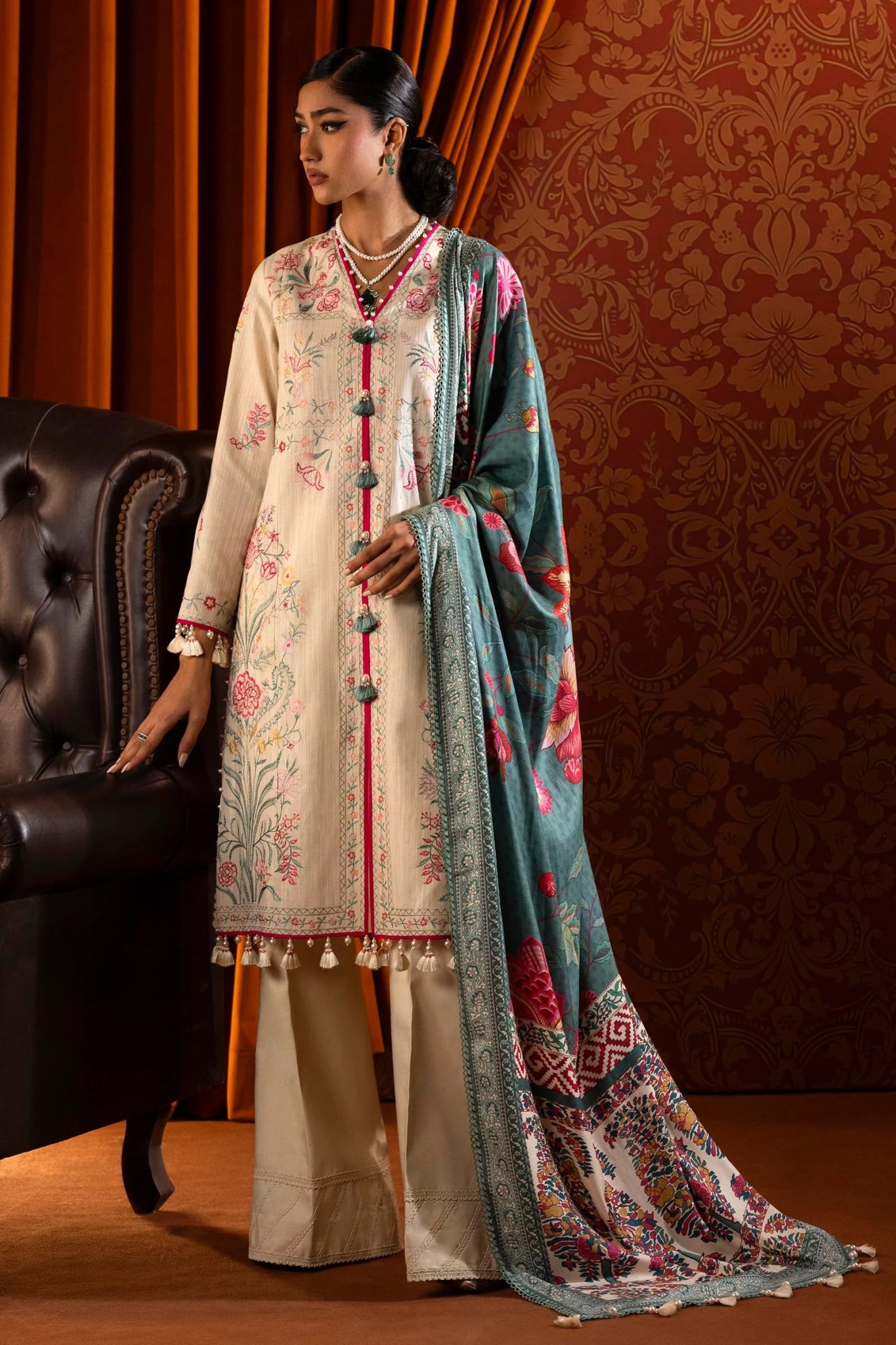 Model wearing a 3 - piece off - white embroidered suit featuring a slub front kali, embroidered sleeves, and a digitally printed shawl with vibrant patterns. Paired with dyed cotton pants, styled gracefully. Part of the Sana Safinaz Muzlin Winter 2024 collection, available online in the UK."