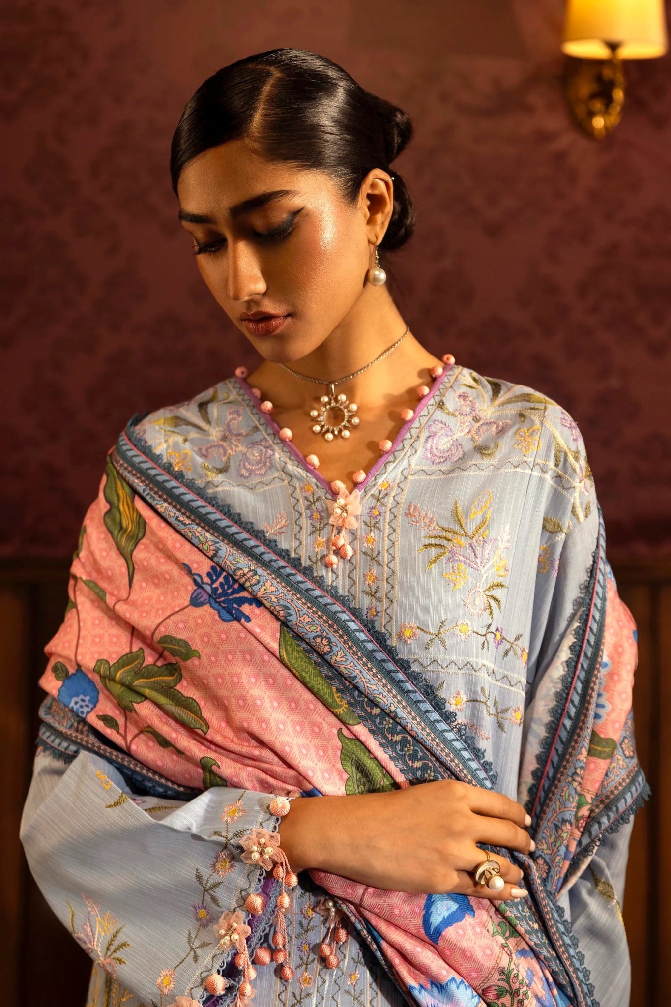 Model wearing a 3 - piece pastel blue embroidered suit featuring a slub front kali, embroidered sleeves, and a digitally printed shawl with floral patterns. Paired with dyed cotton pants for a chic look. Part of the Sana Safinaz Muzlin Winter 2024 collection, available online in the UK