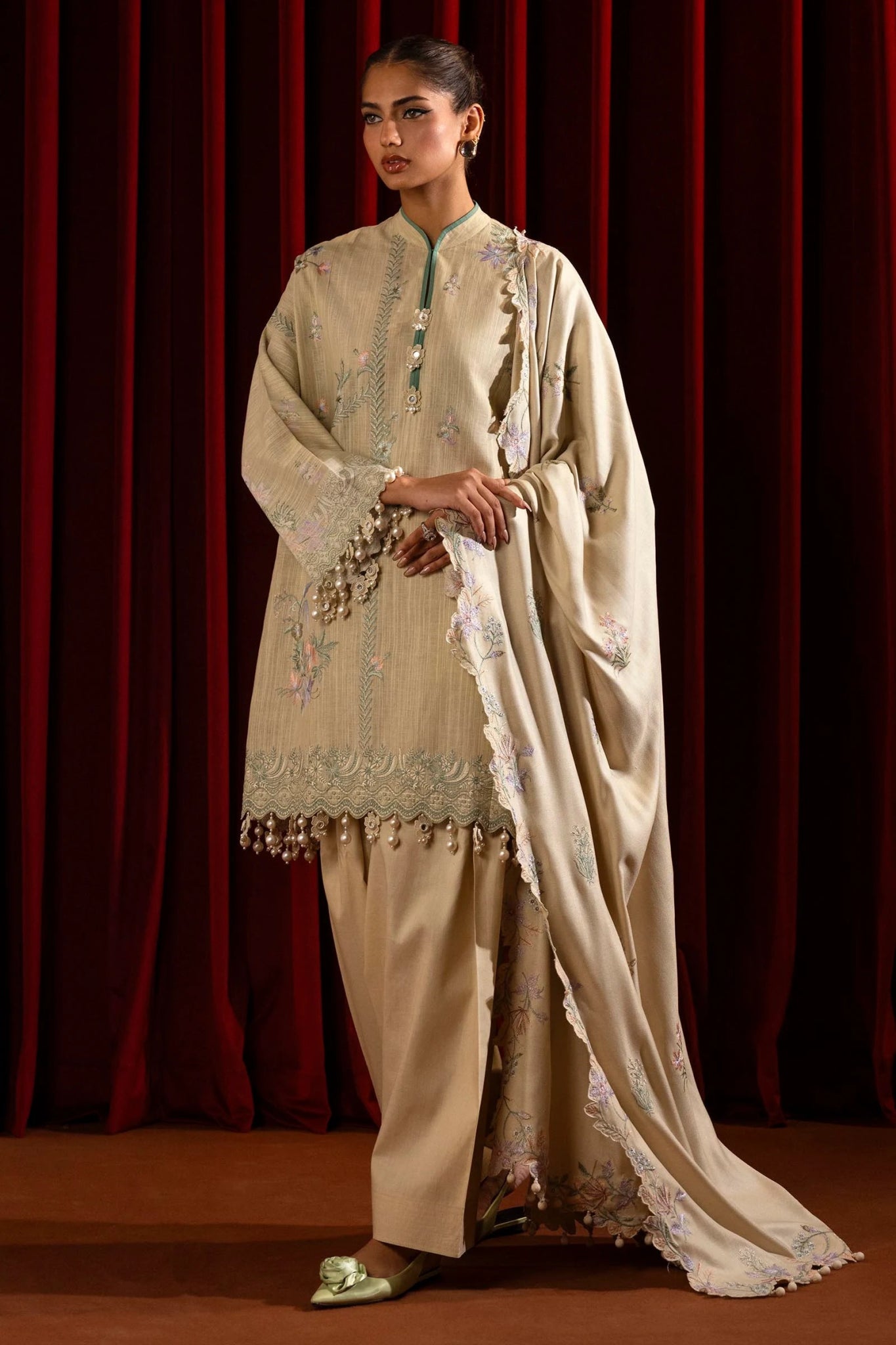 Model wearing a 3 - piece beige embroidered suit featuring a slub front kali, printed back and sleeves, and a shawl with embroidered organza pallu. Paired with dyed cotton pants for an elegant look. Part of the Sana Safinaz Muzlin Winter 2024 collection, available online in the UK.