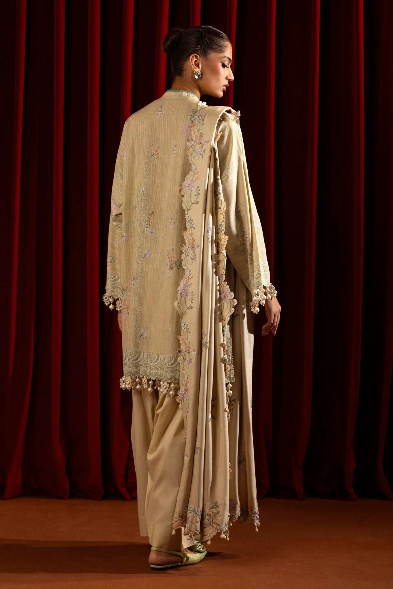 Model wearing a 3 - piece beige embroidered suit featuring a slub front kali, printed back and sleeves, and a shawl with embroidered organza pallu. Paired with dyed cotton pants for an elegant look. Part of the Sana Safinaz Muzlin Winter 2024 collection, available online in the UK.