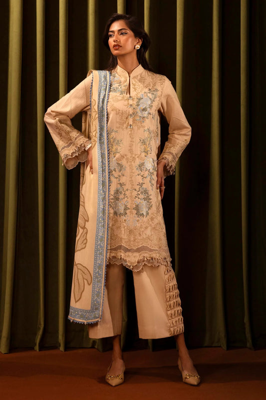 Model wearing a 3 - piece beige embroidered suit featuring a slub front kali, embroidered sleeves with organza details, and a printed shawl with blue borders. Paired with dyed cotton pants for a chic look. Part of the Sana Safinaz Muzlin Winter 2024 collection, available online in the UK.