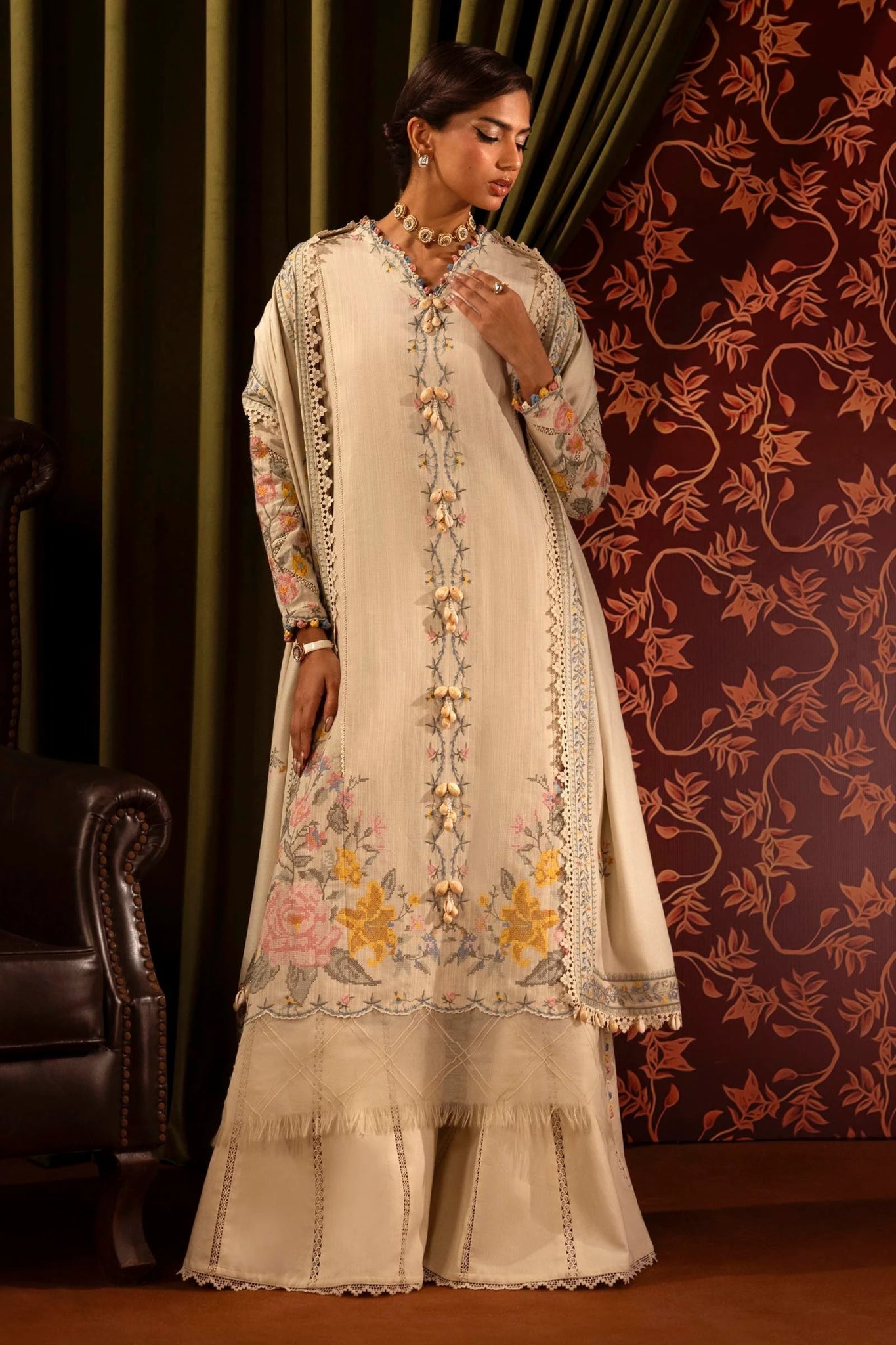 Model wearing a 3 - piece cream embroidered suit featuring a slub front kali, dyed sleeves with organza kuful, and a detailed shawl with embroidered organza pallu. Paired with dyed cotton pants for an elegant look. Part of the Sana Safinaz Muzlin Winter 2024 collection, available online in the UK.