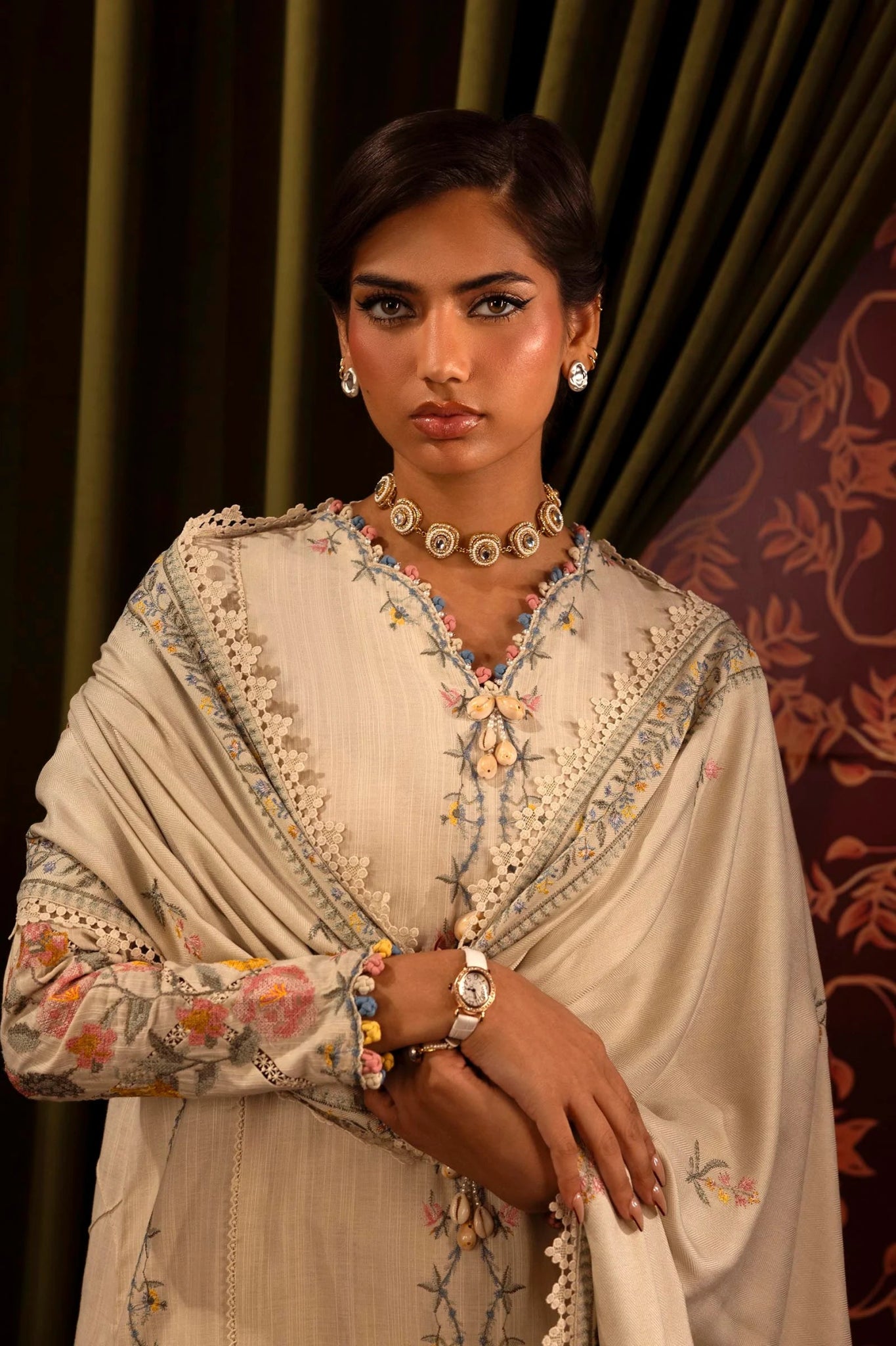 Model wearing a 3 - piece cream embroidered suit featuring a slub front kali, dyed sleeves with organza kuful, and a detailed shawl with embroidered organza pallu. Paired with dyed cotton pants for an elegant look. Part of the Sana Safinaz Muzlin Winter 2024 collection, available online in the UK.