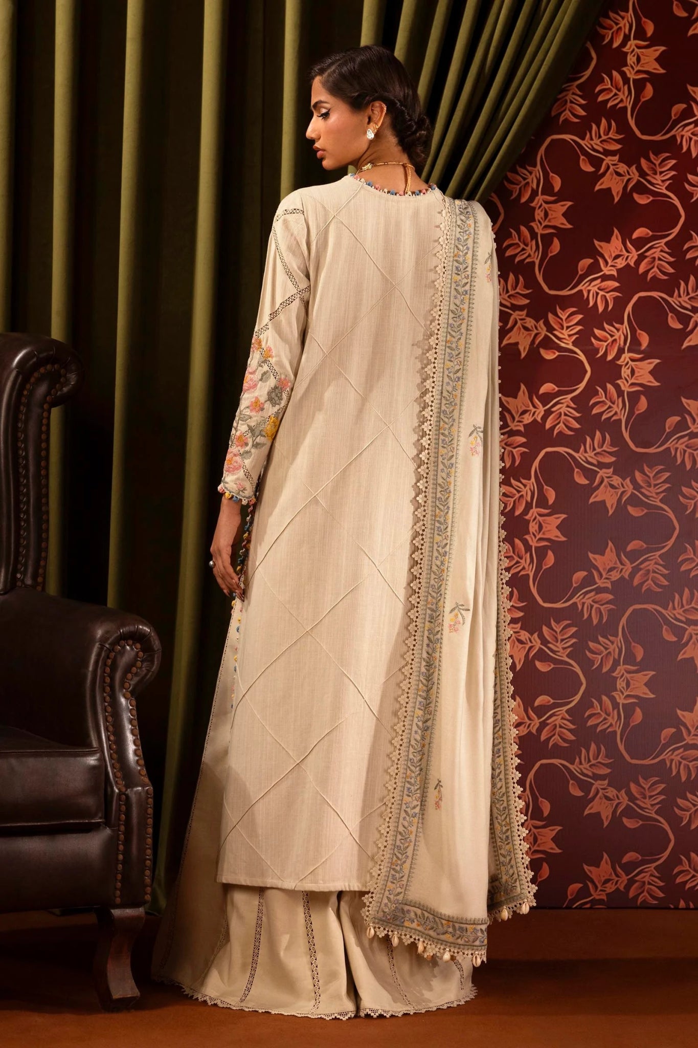 Model wearing a 3 - piece cream embroidered suit featuring a slub front kali, dyed sleeves with organza kuful, and a detailed shawl with embroidered organza pallu. Paired with dyed cotton pants for an elegant look. Part of the Sana Safinaz Muzlin Winter 2024 collection, available online in the UK.