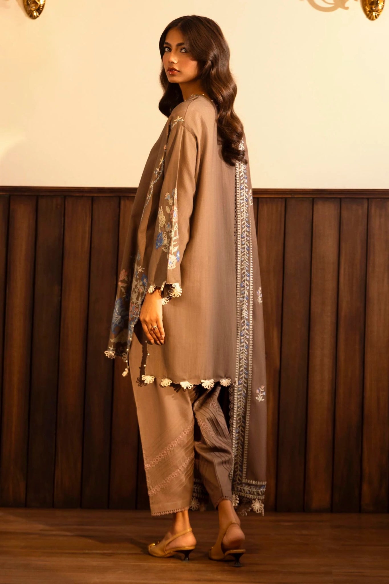 Model wearing a 3 - piece taupe embroidered suit featuring a slub front kali, dyed sleeves with organza kuful, and a shawl with embroidered organza pallu. Paired with dyed cotton pants for an elegant look. Part of the Sana Safinaz Muzlin Winter 2024 collection, available online in the UK.