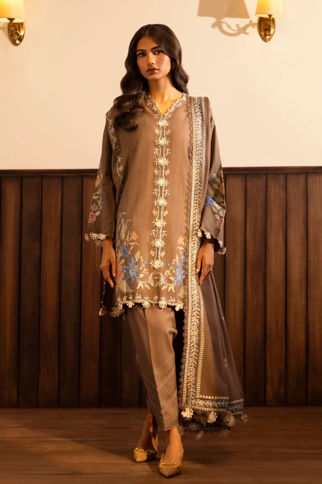 Model wearing a 3 - piece taupe embroidered suit featuring a slub front kali, dyed sleeves with organza kuful, and a shawl with embroidered organza pallu. Paired with dyed cotton pants for an elegant look. Part of the Sana Safinaz Muzlin Winter 2024 collection, available online in the UK.