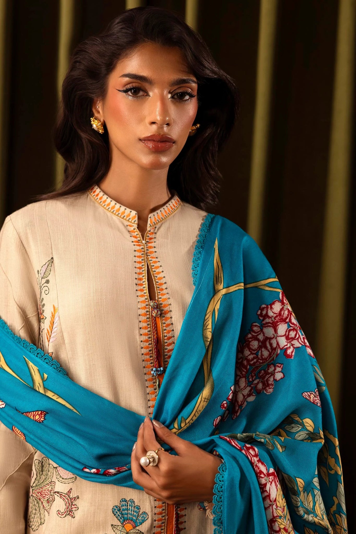 Model wearing a 3 - piece beige embroidered suit featuring a slub front kali, embroidered sleeves, and a vibrant blue printed shawl. Paired with dyed cotton pants for a sophisticated look. Part of the Sana Safinaz Muzlin Winter 2024 collection, available online in the UK