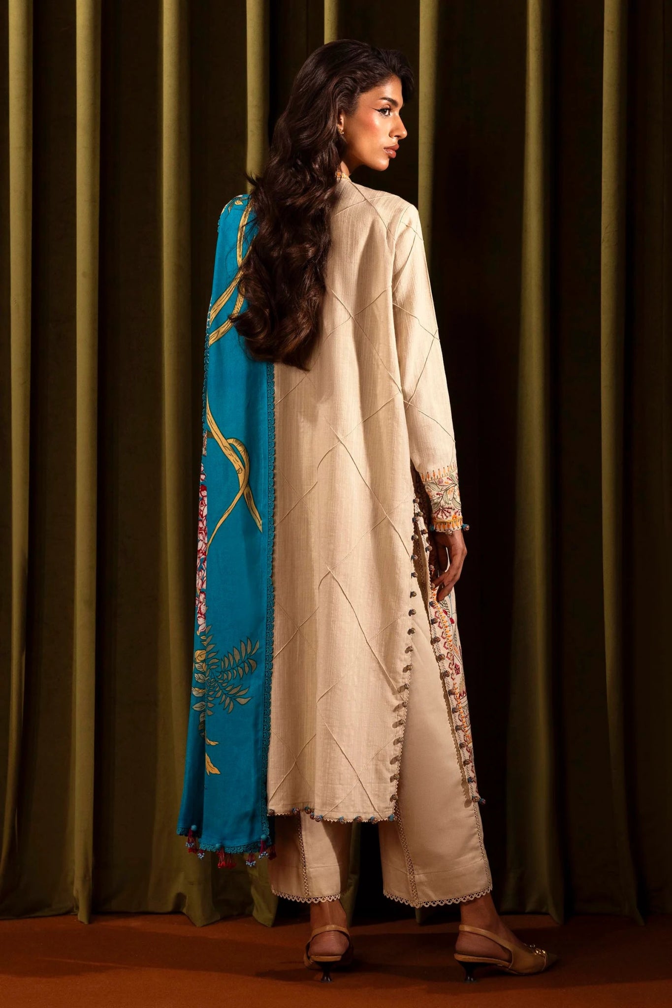 Model wearing a 3 - piece beige embroidered suit featuring a slub front kali, embroidered sleeves, and a vibrant blue printed shawl. Paired with dyed cotton pants for a sophisticated look. Part of the Sana Safinaz Muzlin Winter 2024 collection, available online in the UK