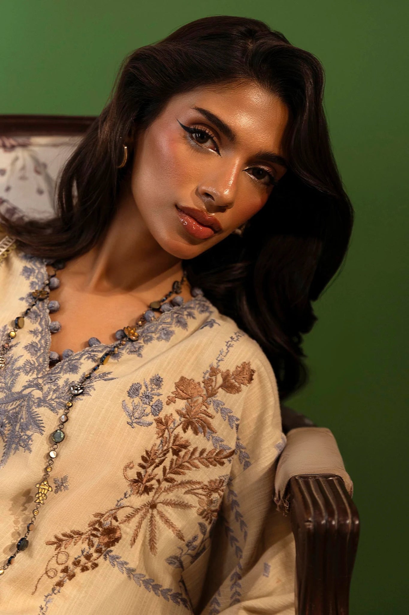 Model wearing a 3 - piece beige embroidered suit featuring a slub front kali, printed back and sleeves, and a digital printed shawl with bold floral patterns. Paired with dyed cotton pants for an elegant look. Part of the Sana Safinaz Muzlin Winter 2024 collection, available online in the UK.