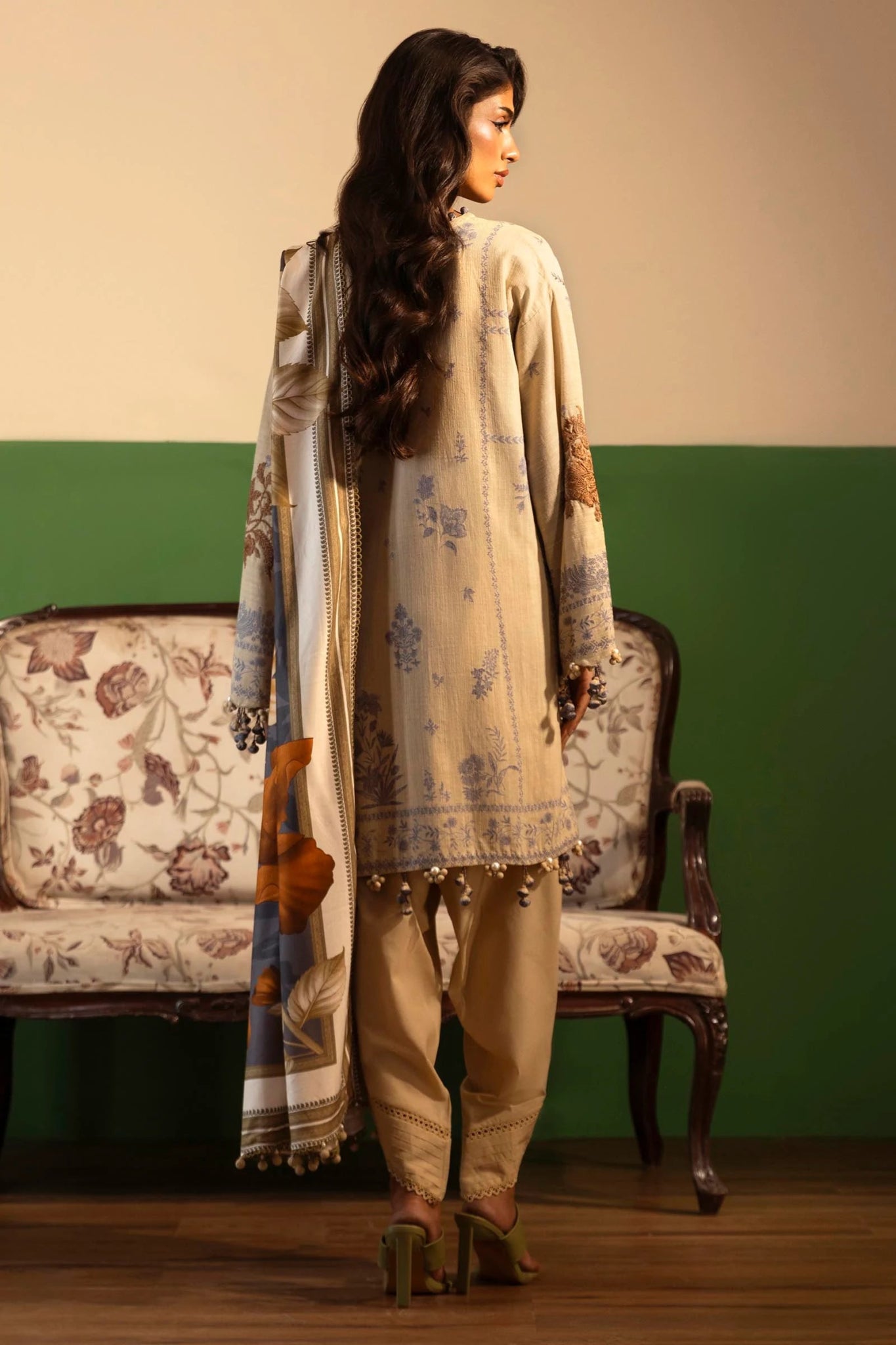 Model wearing a 3 - piece beige embroidered suit featuring a slub front kali, printed back and sleeves, and a digital printed shawl with bold floral patterns. Paired with dyed cotton pants for an elegant look. Part of the Sana Safinaz Muzlin Winter 2024 collection, available online in the UK.