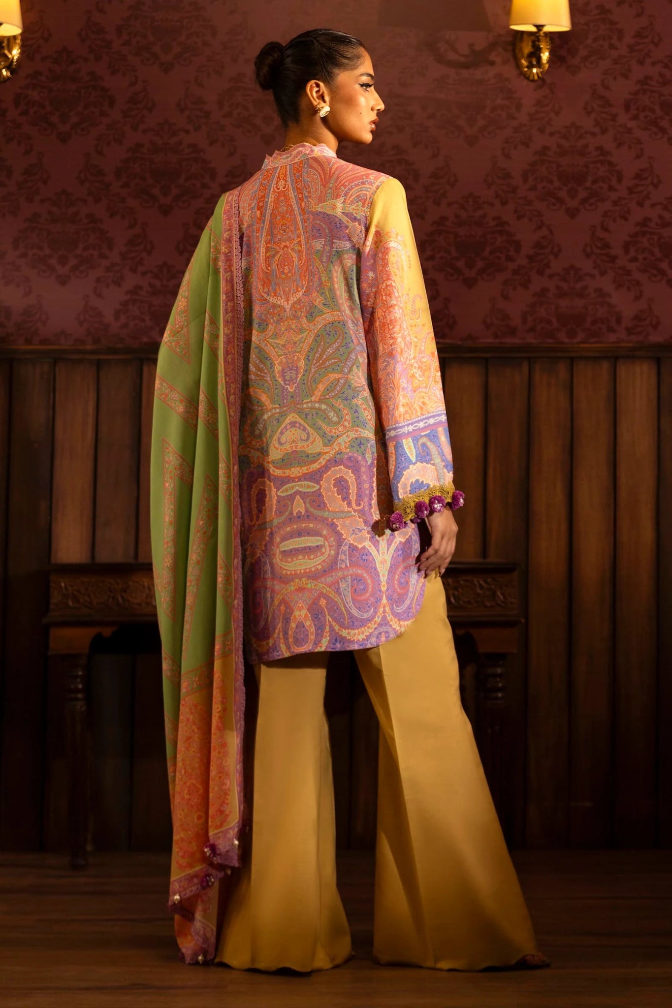 Model wearing a 3 - piece vibrant yellow suit featuring a digitally printed linen front, back, and sleeves, paired with a colorful printed dupatta. Styled with dyed cotton pants for a bold look. Part of the Sana Safinaz Muzlin Winter 2024 collection, available online in the UK.