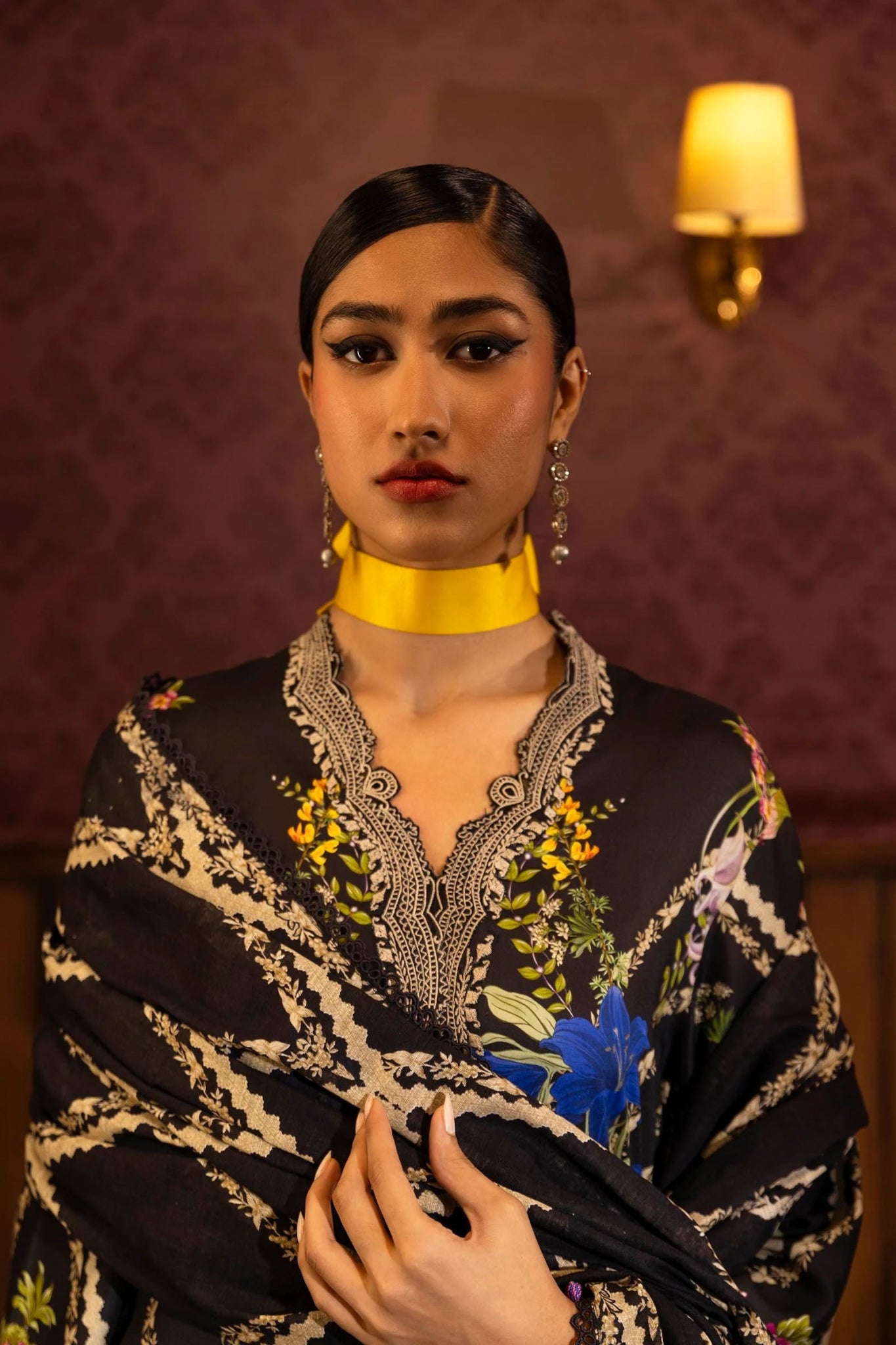 Model wearing a 3 - piece black suit featuring a digitally printed linen front, back, and sleeves with vibrant floral patterns. Styled with an embroidered organza neckline and border, a printed khaddar dupatta, and dyed cotton pants for an elegant look. Part of the Sana Safinaz Muzlin Winter 2024 collection, available online in the UK.