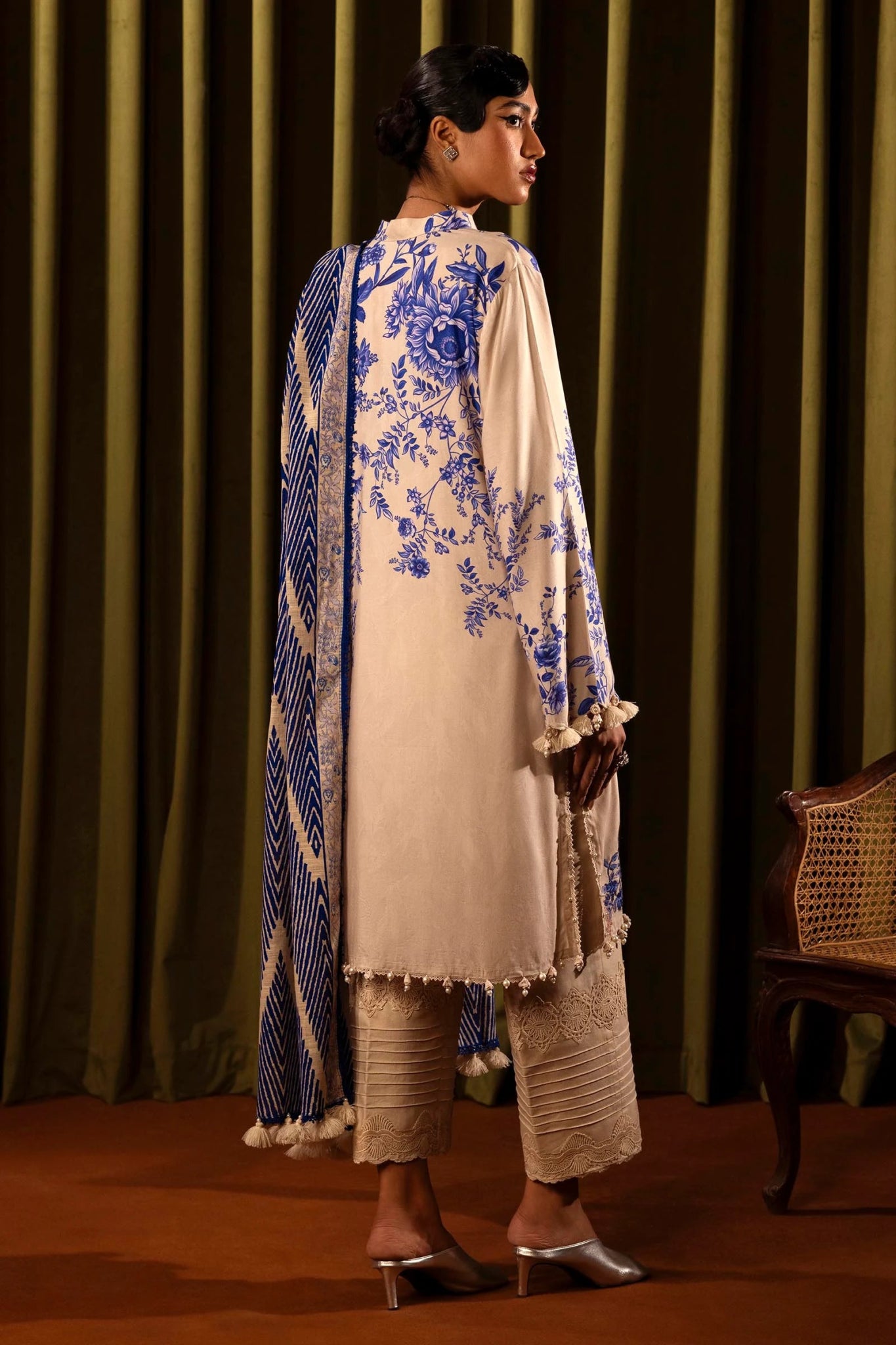 Model wearing a 3 - piece cream suit featuring a digitally printed linen front, back, and sleeves with blue floral patterns. Styled with an embroidered organza daman, a printed khaddar dupatta, and dyed cotton pants for a refined look. Part of the Sana Safinaz Muzlin Winter 2024 collection, available online in the UK.