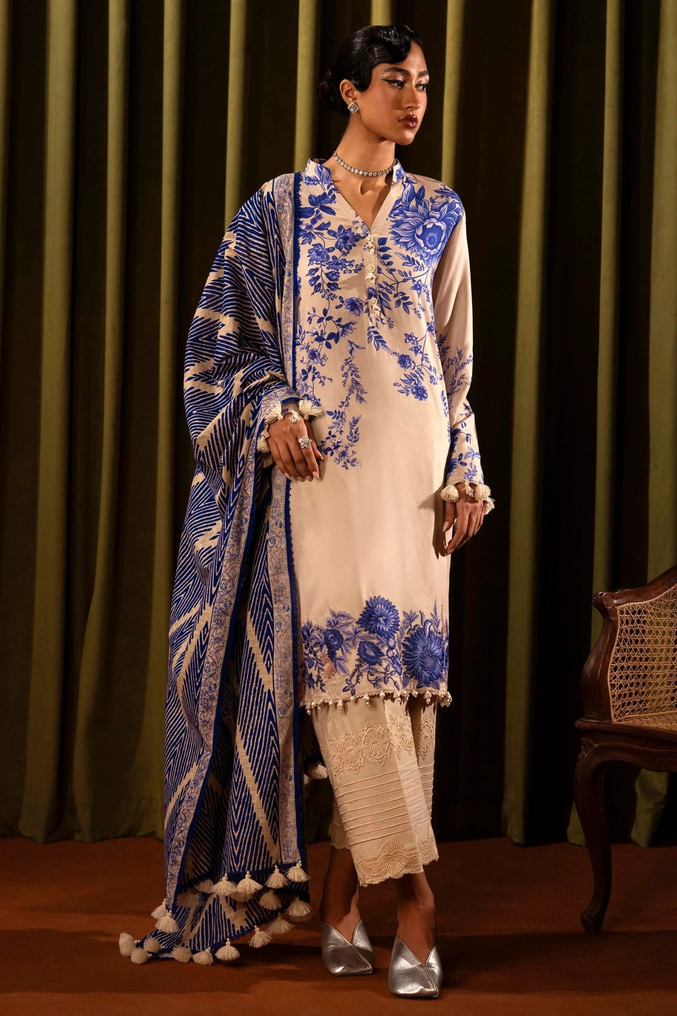 Model wearing a 3 - piece cream suit featuring a digitally printed linen front, back, and sleeves with blue floral patterns. Styled with an embroidered organza daman, a printed khaddar dupatta, and dyed cotton pants for a refined look. Part of the Sana Safinaz Muzlin Winter 2024 collection, available online in the UK.