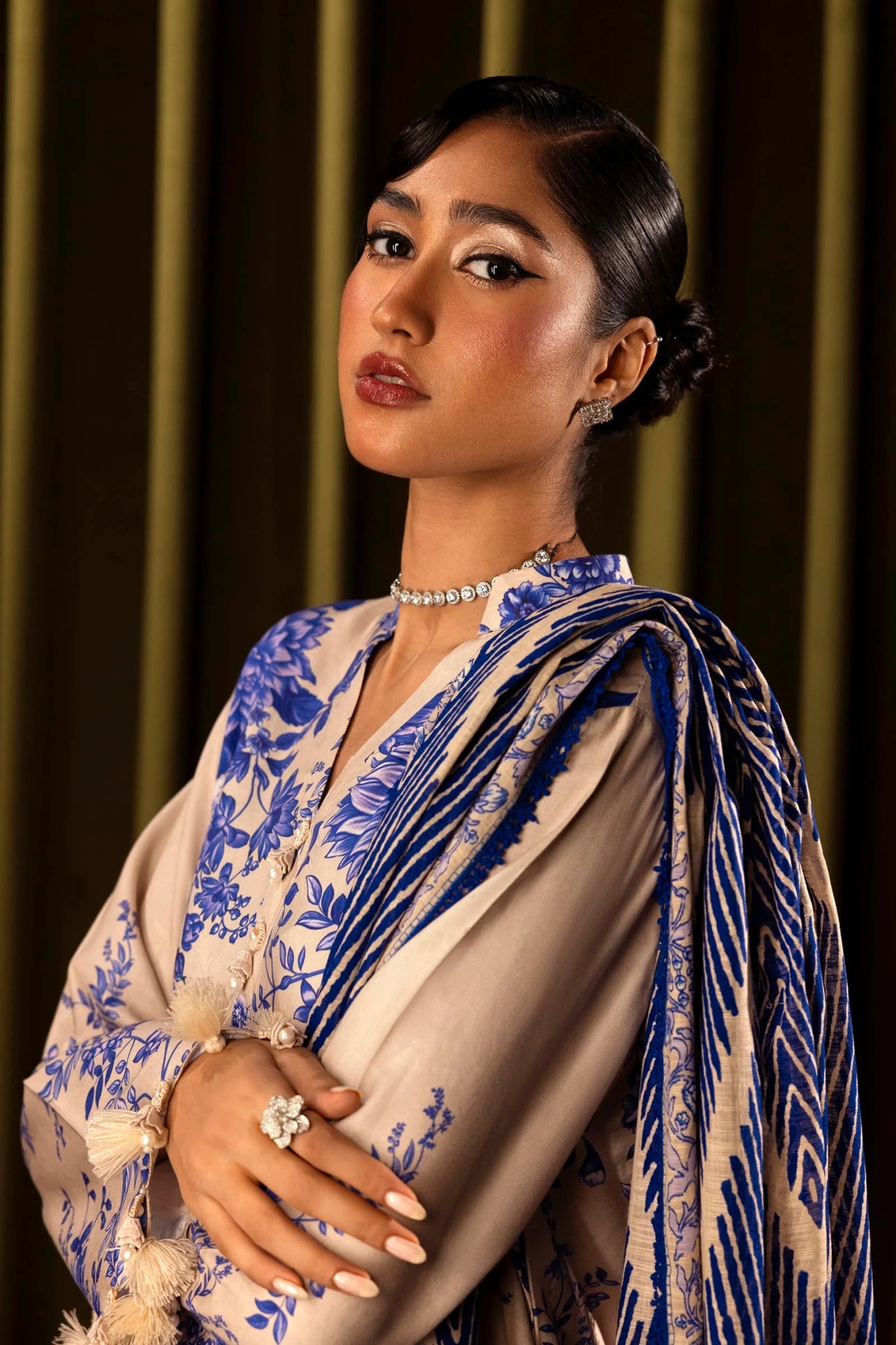 Model wearing a 3 - piece cream suit featuring a digitally printed linen front, back, and sleeves with blue floral patterns. Styled with an embroidered organza daman, a printed khaddar dupatta, and dyed cotton pants for a refined look. Part of the Sana Safinaz Muzlin Winter 2024 collection, available online in the UK.