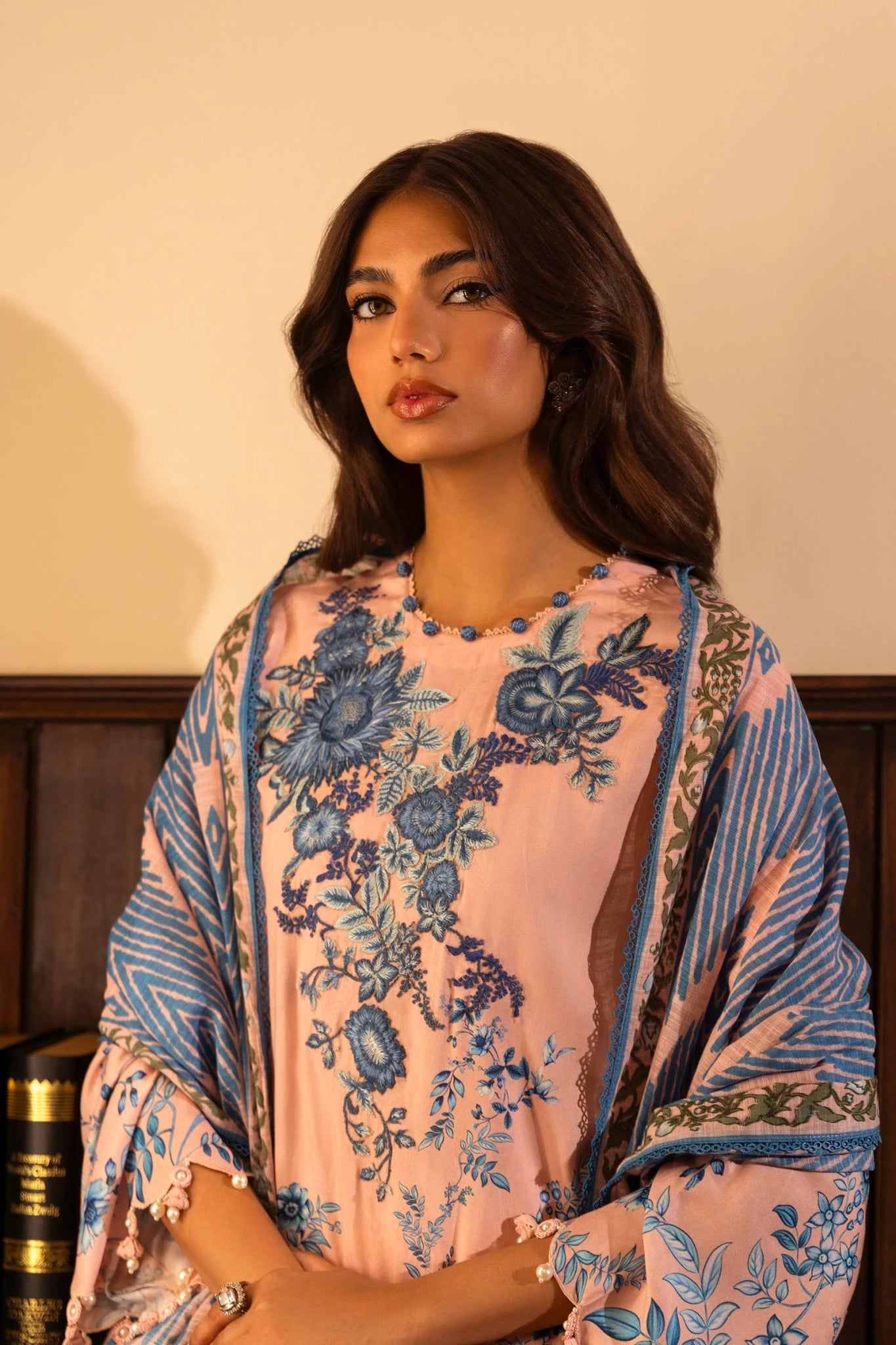 Model wearing a 3 - piece pink suit featuring a digitally printed linen front, back, and sleeves with blue floral patterns. Styled with an embroidered organza daman, a printed khaddar dupatta, and dyed cotton pants for a chic look. Part of the Sana Safinaz Muzlin Winter 2024 collection, available online in the UK.