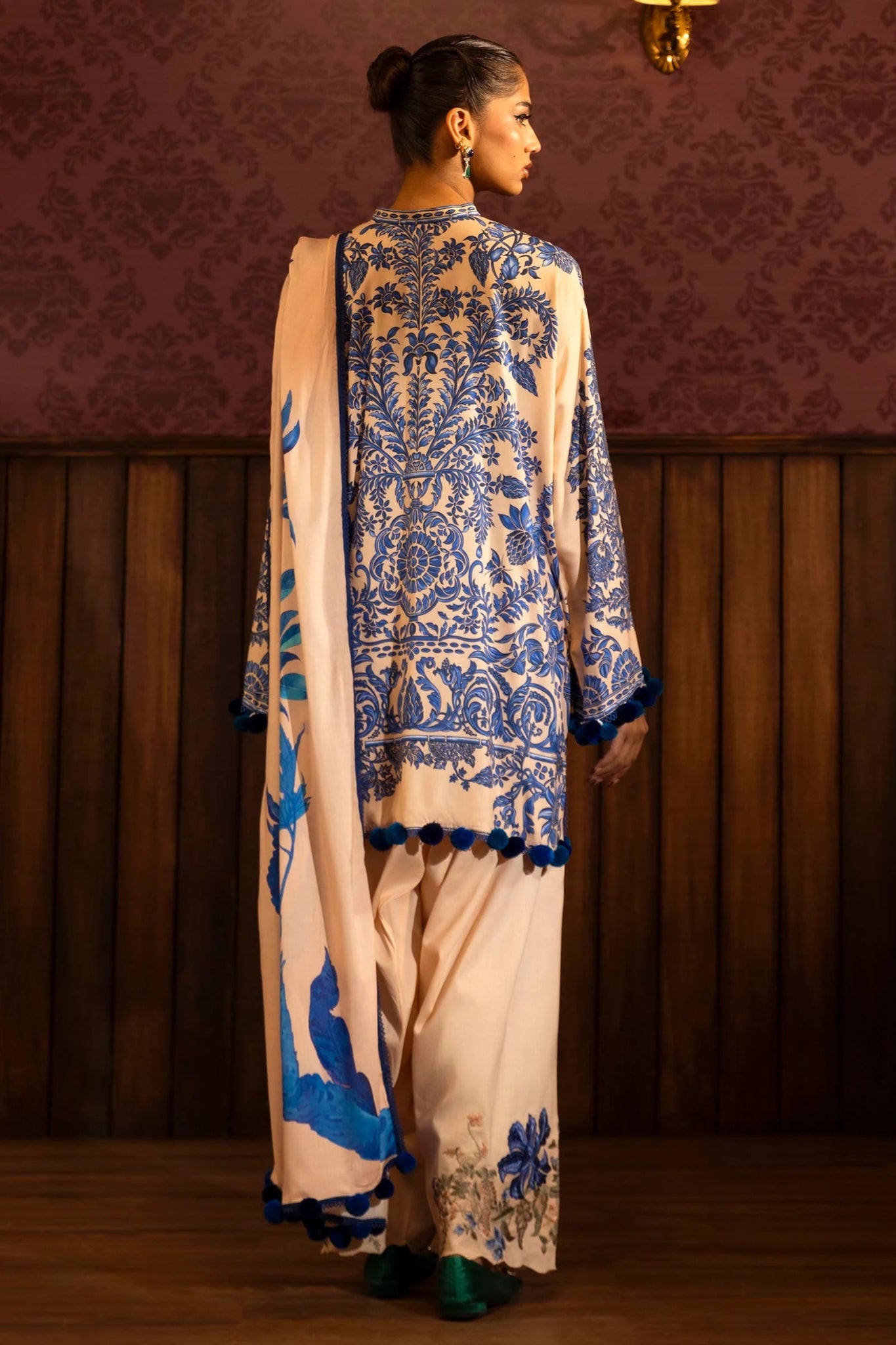 Model wearing a 3 - piece cream and blue suit featuring a digitally printed linen front, back, and sleeves with intricate patterns. Styled with embroidered organza sleeve borders, a printed linen dupatta, and dyed cotton pants with floral embroidery. Part of the Sana Safinaz Muzlin Winter 2024 collection, available online in the UK.