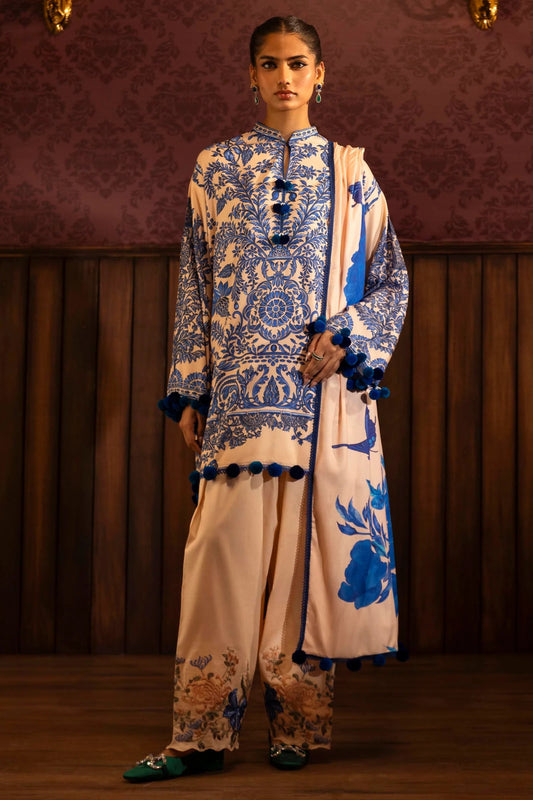 Model wearing a 3 - piece cream and blue suit featuring a digitally printed linen front, back, and sleeves with intricate patterns. Styled with embroidered organza sleeve borders, a printed linen dupatta, and dyed cotton pants with floral embroidery. Part of the Sana Safinaz Muzlin Winter 2024 collection, available online in the UK.