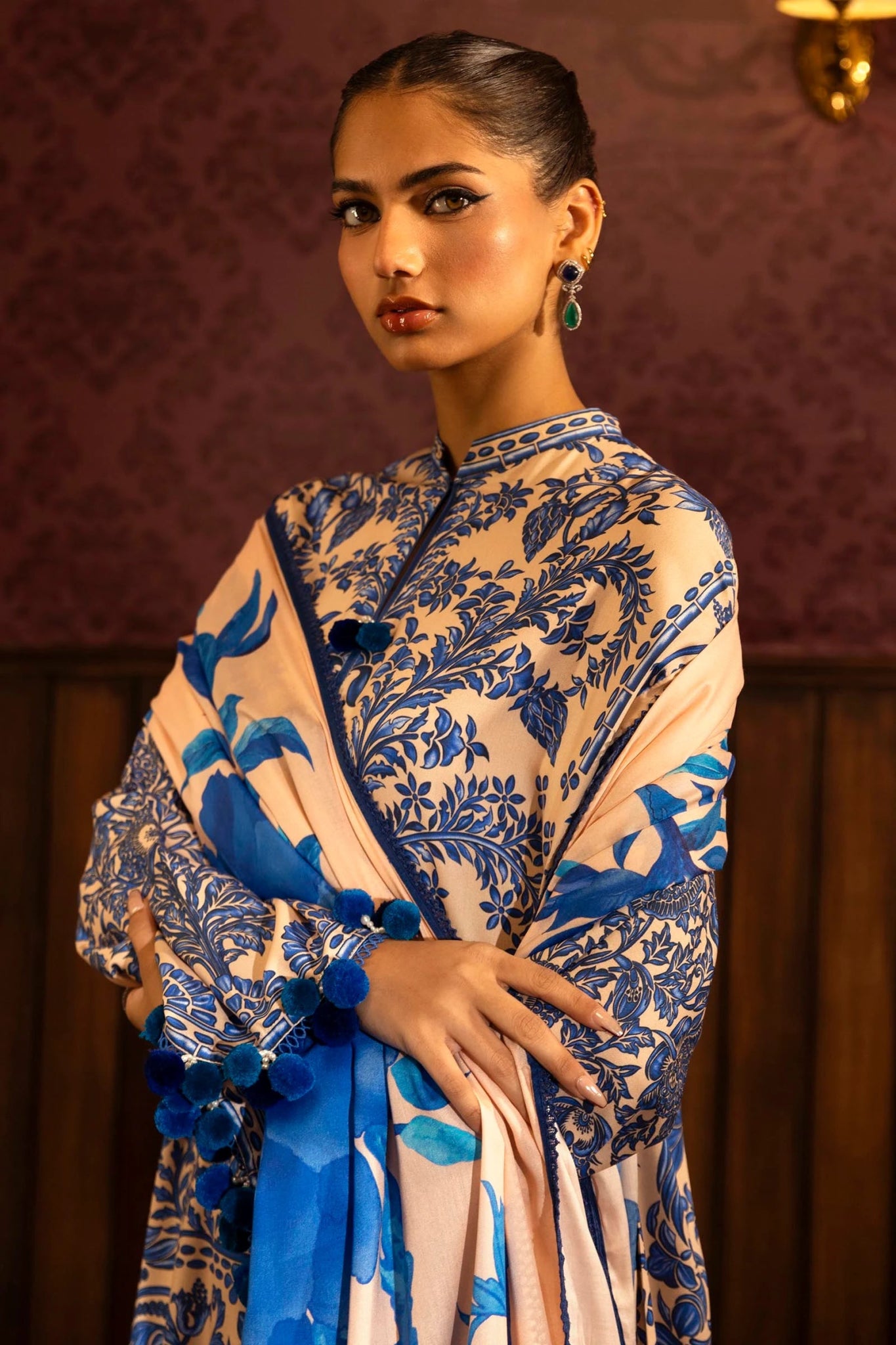 Model wearing a 3 - piece cream and blue suit featuring a digitally printed linen front, back, and sleeves with intricate patterns. Styled with embroidered organza sleeve borders, a printed linen dupatta, and dyed cotton pants with floral embroidery. Part of the Sana Safinaz Muzlin Winter 2024 collection, available online in the UK.