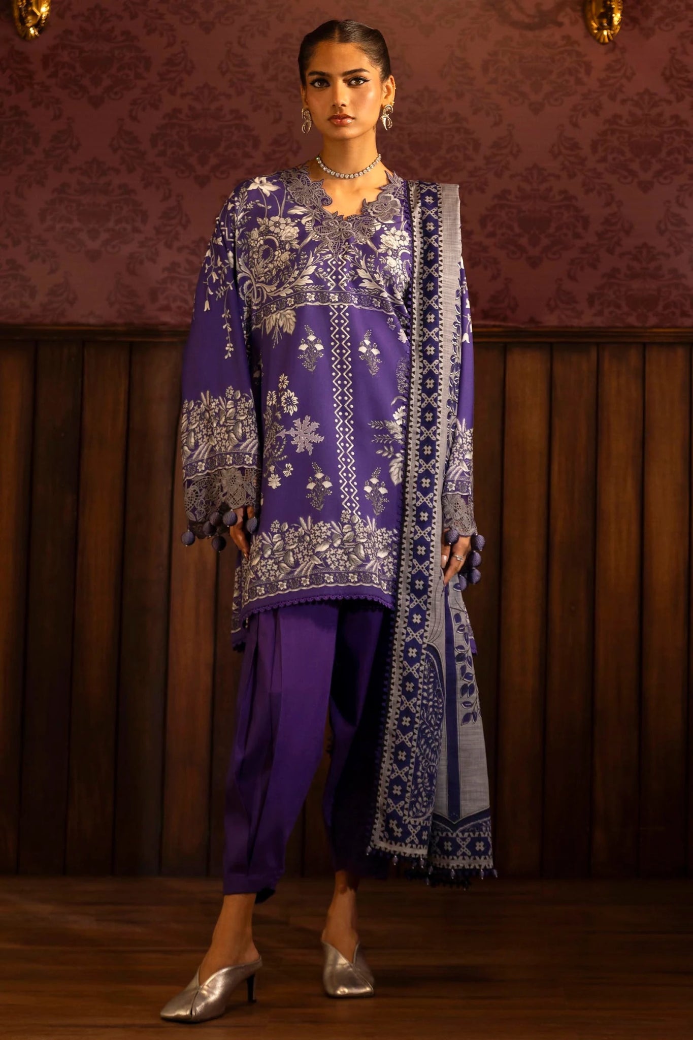 Model wearing a 3 - piece deep purple suit featuring a digitally printed linen front, back, and sleeves with intricate patterns. Styled with an embroidered organza neckline and border, a printed khaddar dupatta, and dyed cotton pants for an elegant look. Part of the Sana Safinaz Muzlin Winter 2024 collection, available online in the UK.