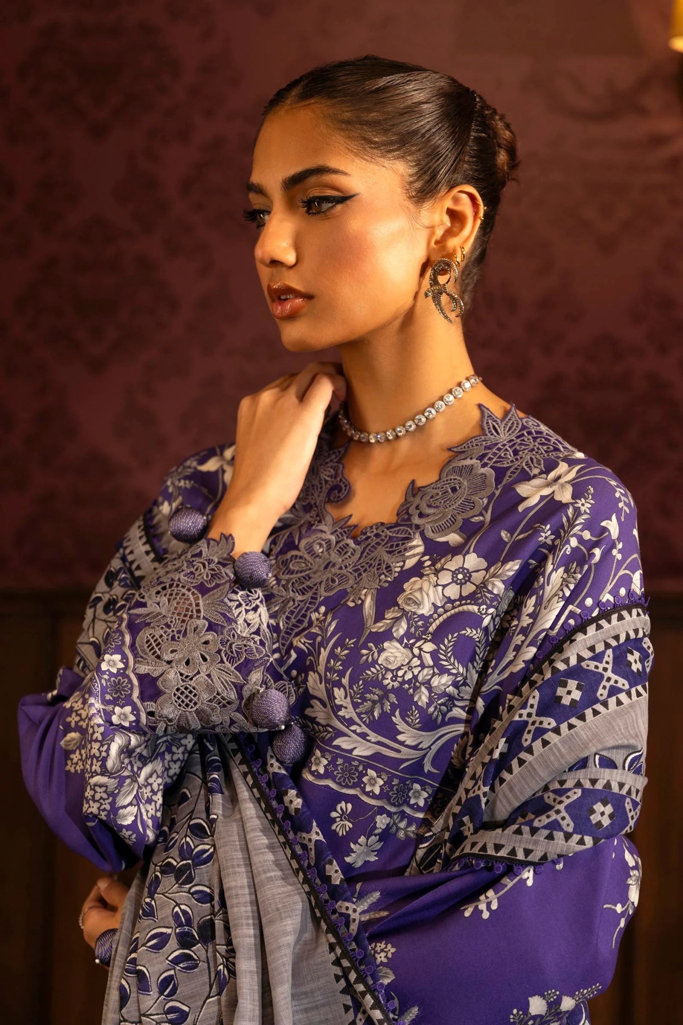 Model wearing a 3 - piece deep purple suit featuring a digitally printed linen front, back, and sleeves with intricate patterns. Styled with an embroidered organza neckline and border, a printed khaddar dupatta, and dyed cotton pants for an elegant look. Part of the Sana Safinaz Muzlin Winter 2024 collection, available online in the UK.