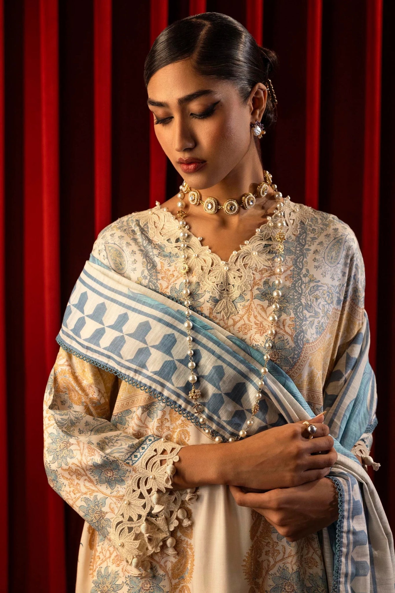 Model wearing a 3 - piece cream suit featuring a digitally printed linen front, back, and sleeves with blue and golden accents. Styled with an embroidered organza neckline and sleeve borders, a printed khaddar dupatta, and dyed cotton pants for an elegant look. Part of the Sana Safinaz Muzlin Winter 2024 collection, available online in the UK.