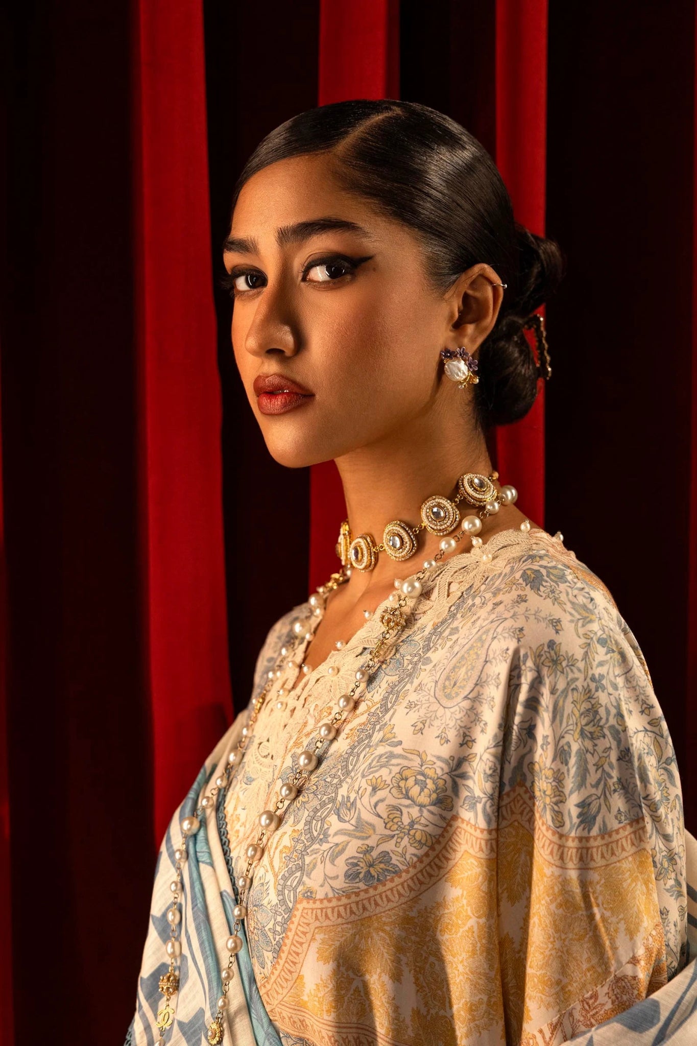 Model wearing a 3 - piece cream suit featuring a digitally printed linen front, back, and sleeves with blue and golden accents. Styled with an embroidered organza neckline and sleeve borders, a printed khaddar dupatta, and dyed cotton pants for an elegant look. Part of the Sana Safinaz Muzlin Winter 2024 collection, available online in the UK.