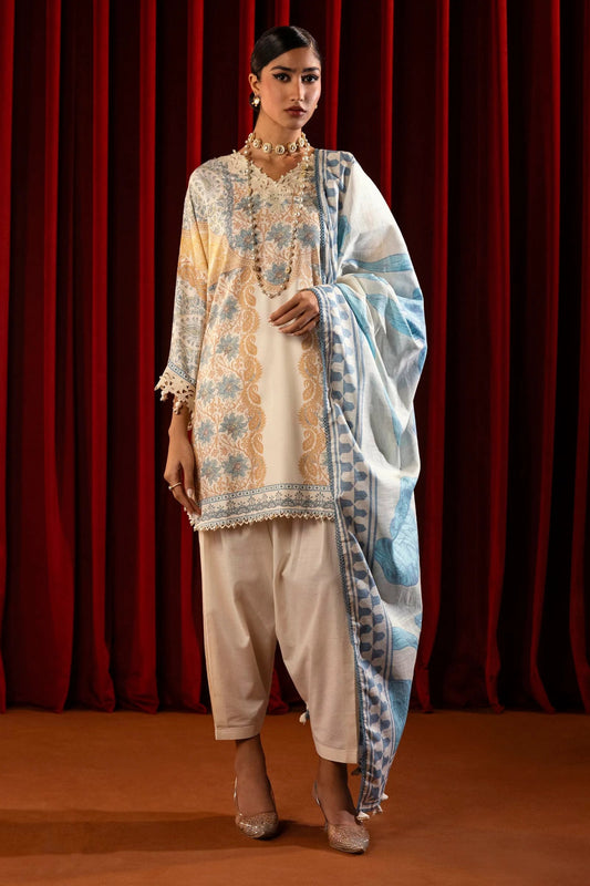 Model wearing a 3 - piece cream suit featuring a digitally printed linen front, back, and sleeves with blue and golden accents. Styled with an embroidered organza neckline and sleeve borders, a printed khaddar dupatta, and dyed cotton pants for an elegant look. Part of the Sana Safinaz Muzlin Winter 2024 collection, available online in the UK.