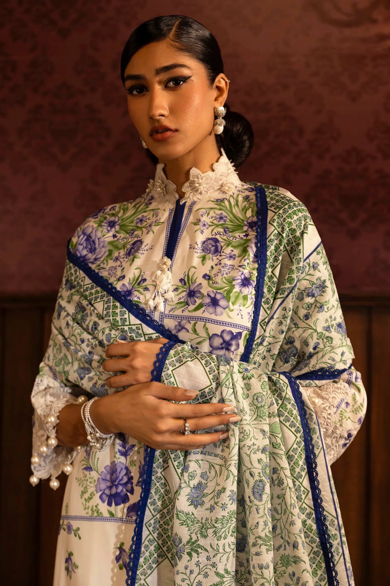 Model wearing a floral 3 - piece suit from Sana Safinaz Muzlin Winter 2024 collection, featuring digital printed linen front, back, and sleeves with embroidered neckline and sleeves, paired with a khaddar dupatta and dyed cotton pants.